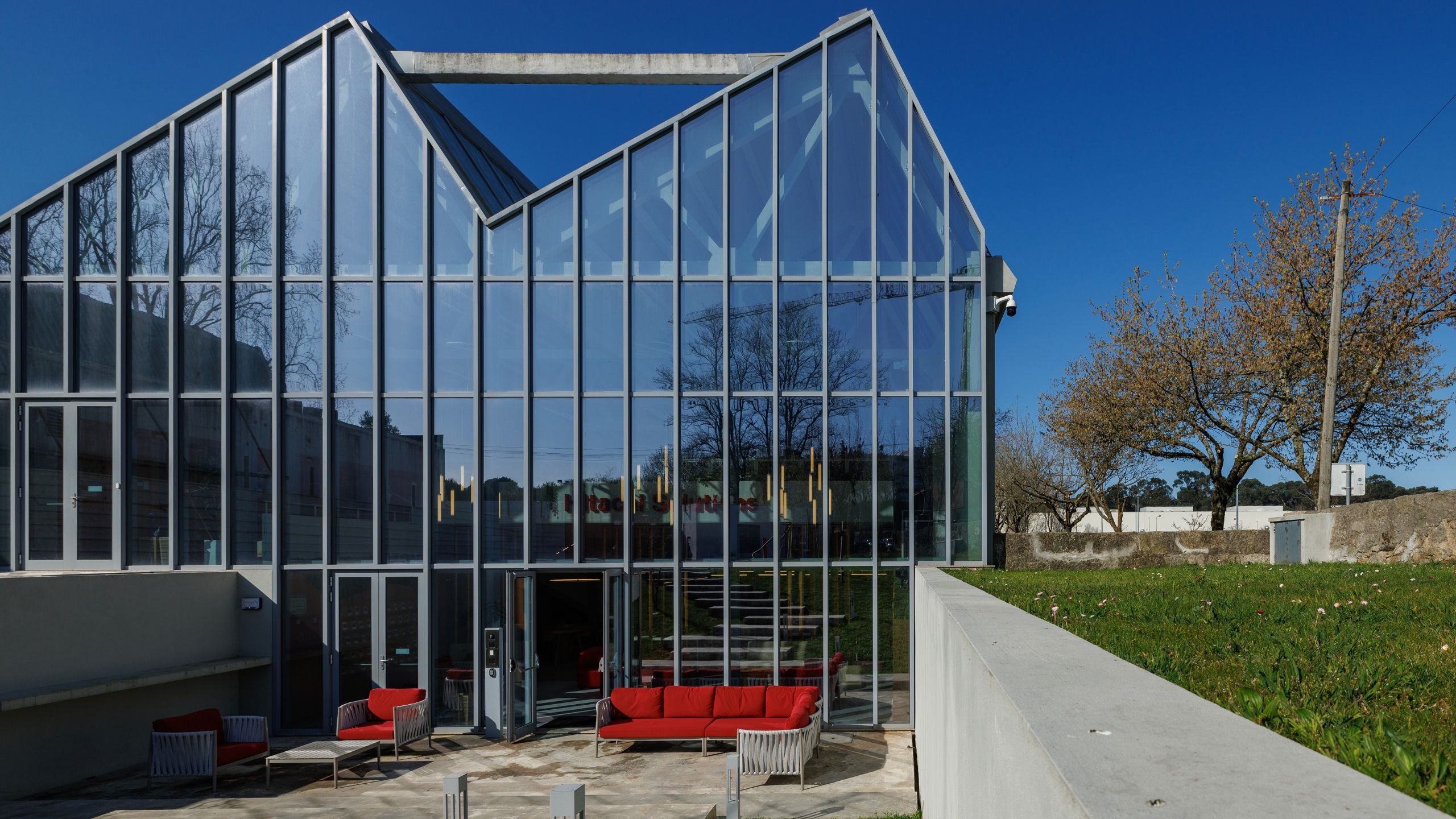 Zona exterior do escritório com pátio afundado, sofás vermelhos, fachada envidraçada e área ajardinada de inspiração num Jardim Zen.