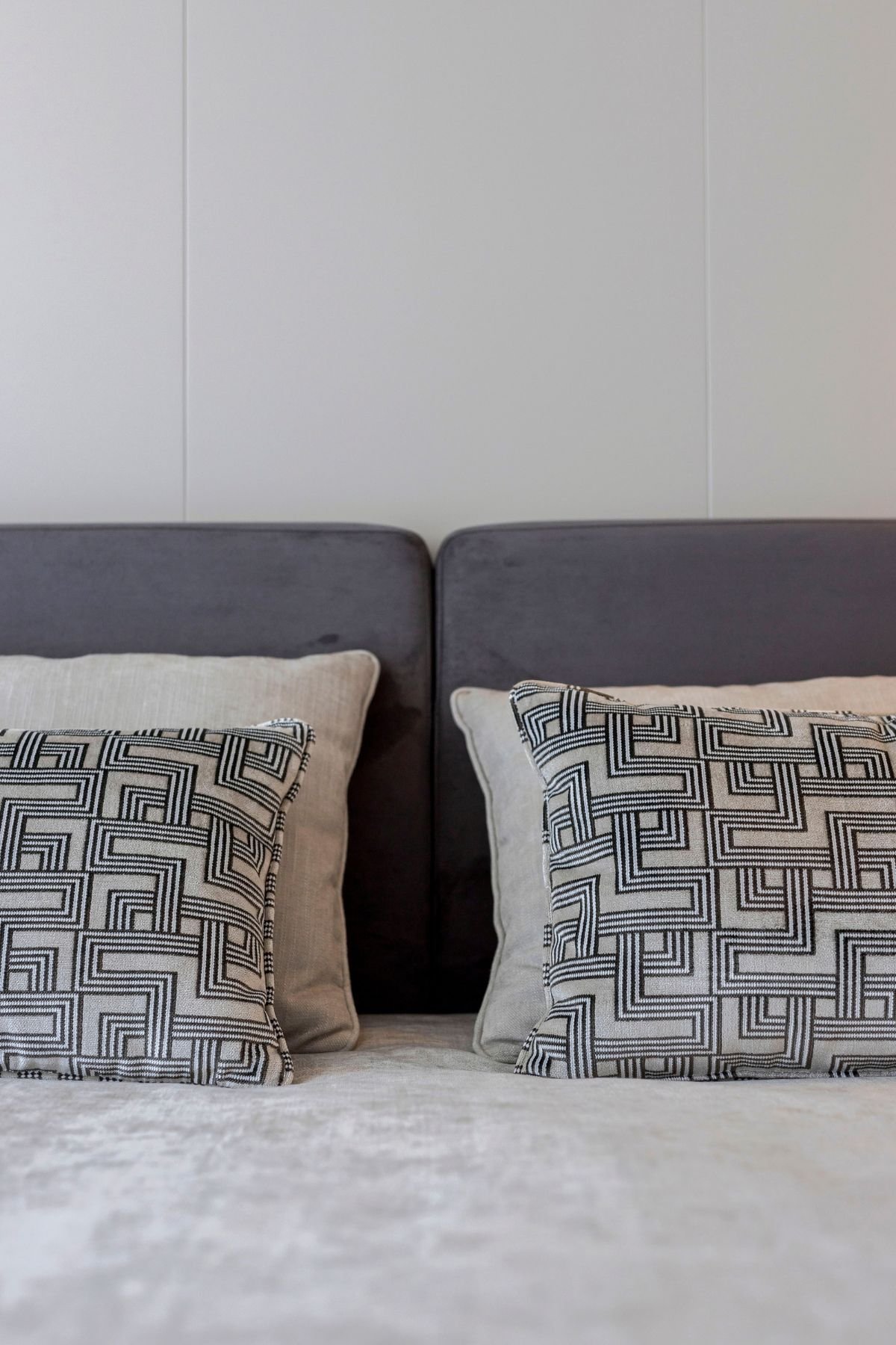 Pormenor de almofadas com padrão geométrico sobre cama num quarto de casal decorado, destacando os têxteis de interior design e decoração de quarto em casas modernas.