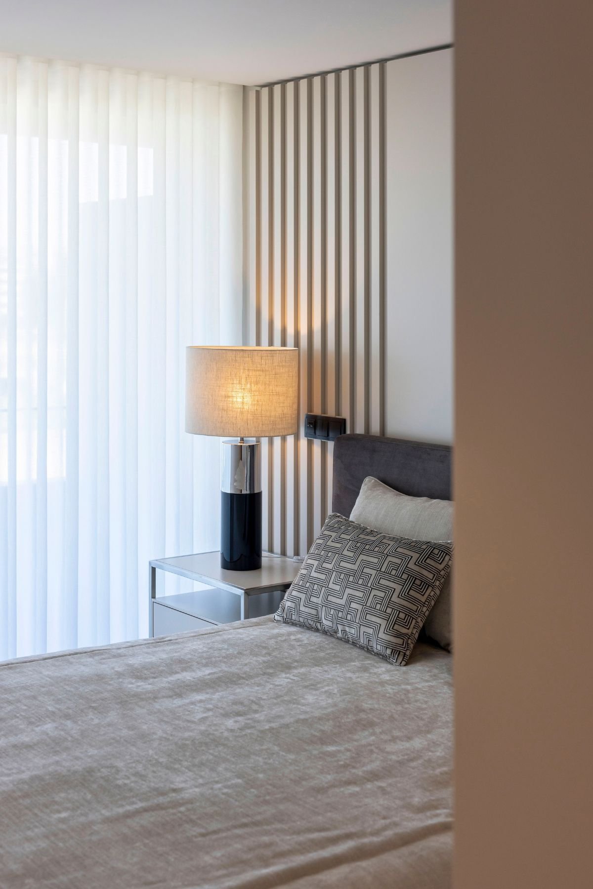 Cama acolhedora e iluminação suave num quarto de casal decorado com detalhes em madeira, inspirado no melhor do interior design e decoração de quarto em casas modernas.