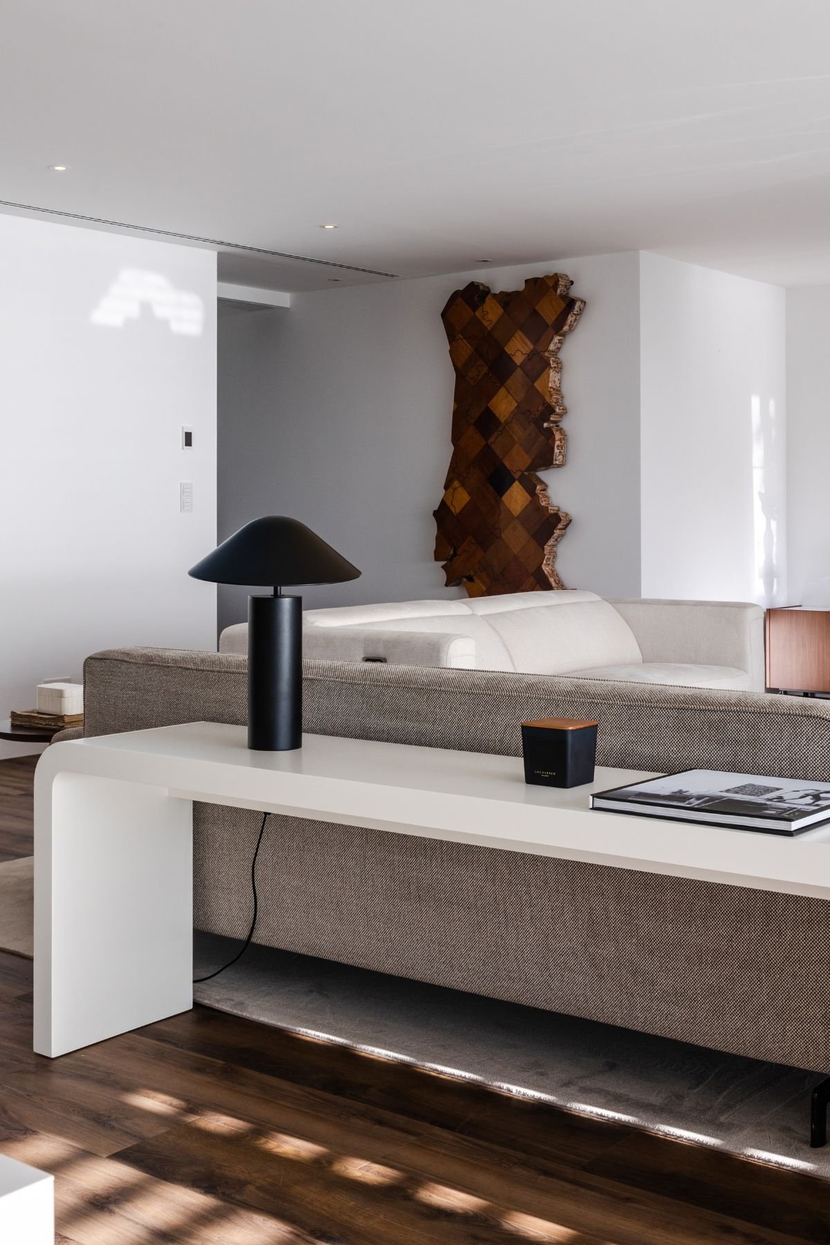 Detalhe do móvel consola branco com candeeiro de mesa preto posicionado atrás do sofá.