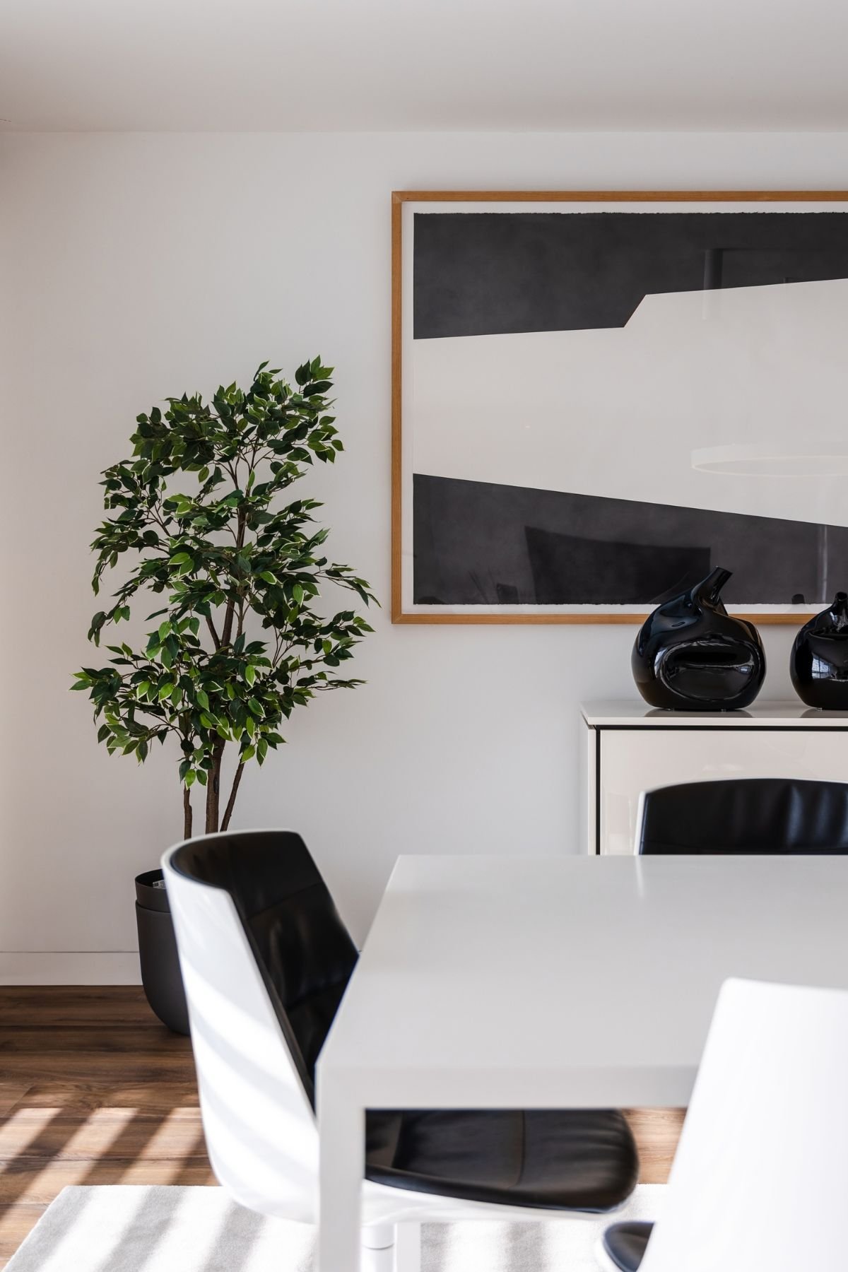 Plano aproximado do topo da mesa junto à planta decorativa, destacando a consola branca e o quadro abstrato em tons de preto e branco.