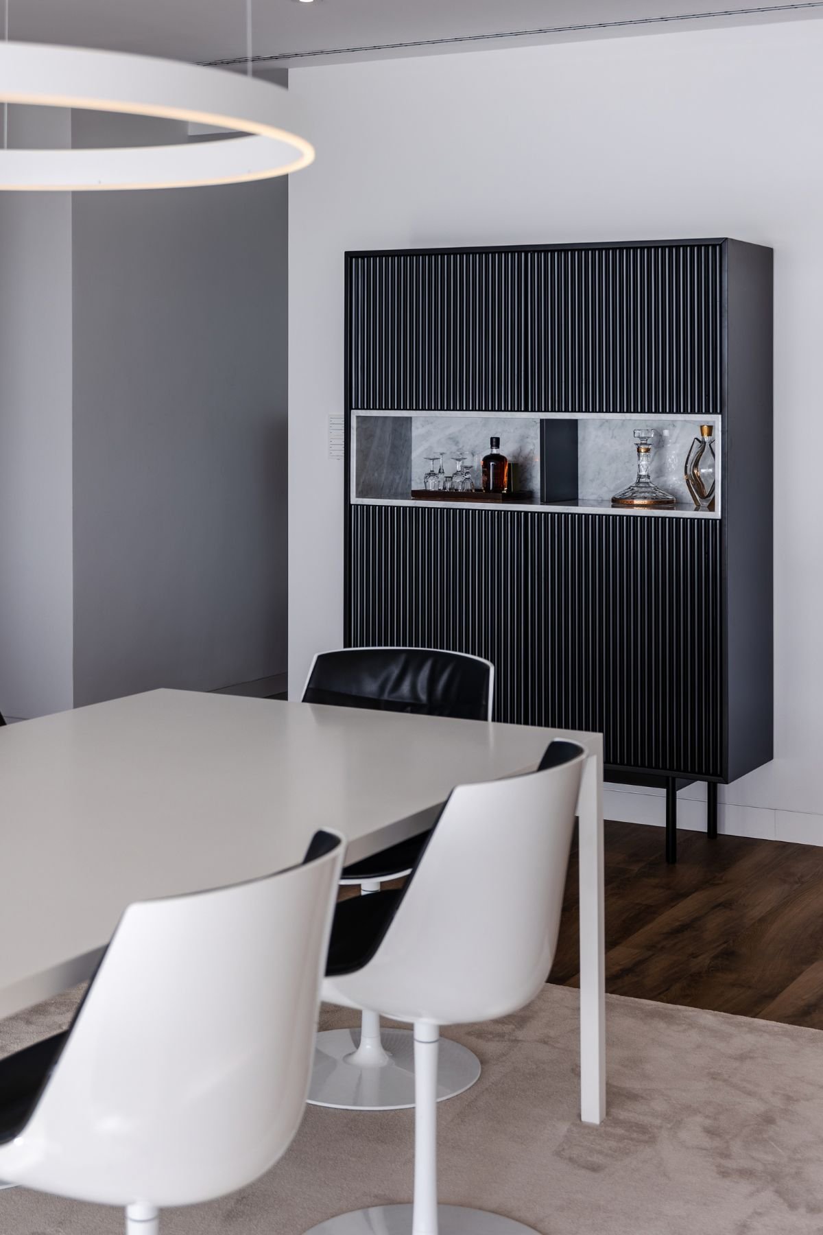 Primeiro plano do móvel bar preto com superfície canelada e nicho aberto com iluminação interna para garrafas e copos.