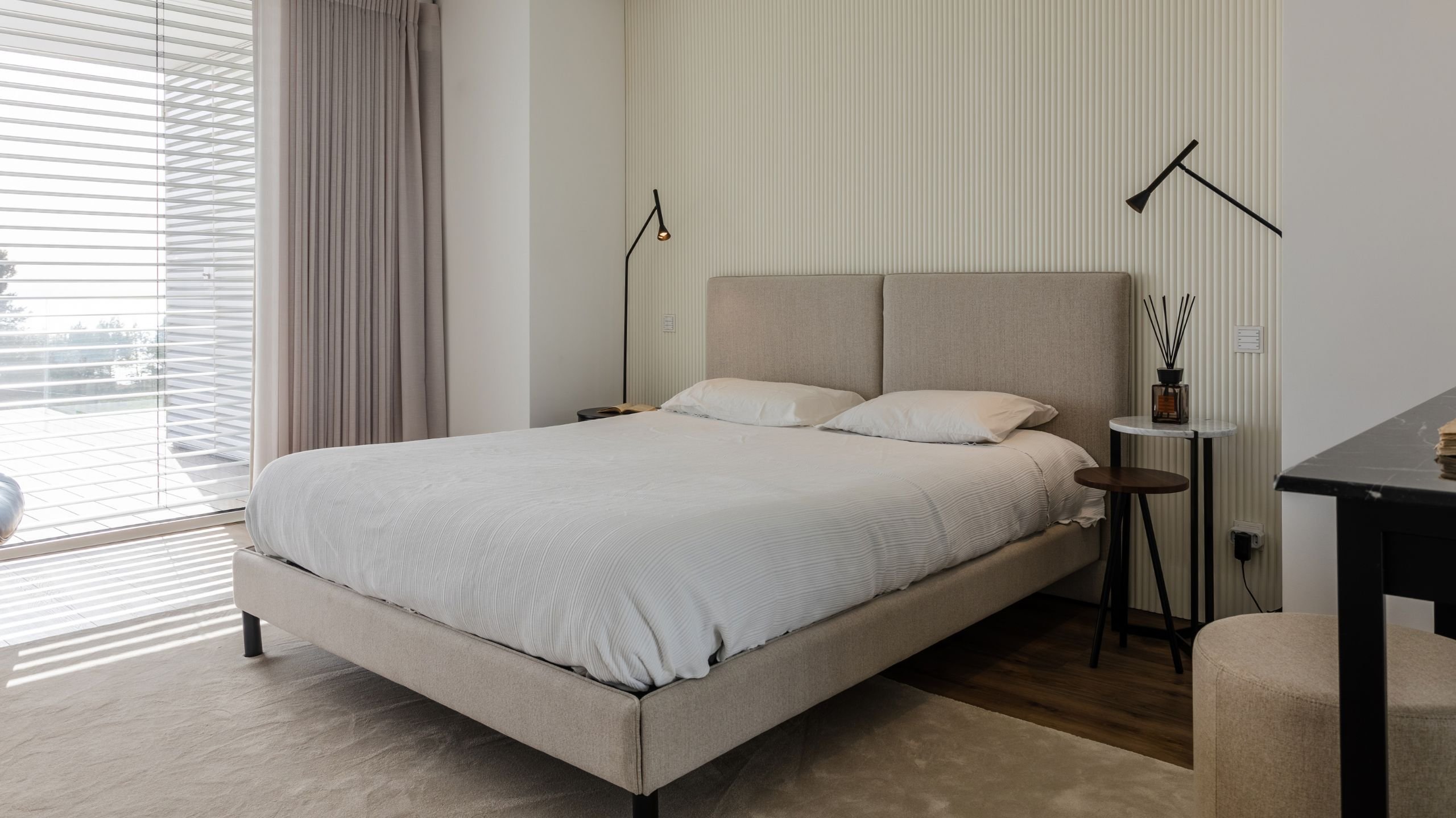 Vista em perspetiva da cama simples de tecido estofado, realçando os painéis ripados brancos no fundo da parede.
