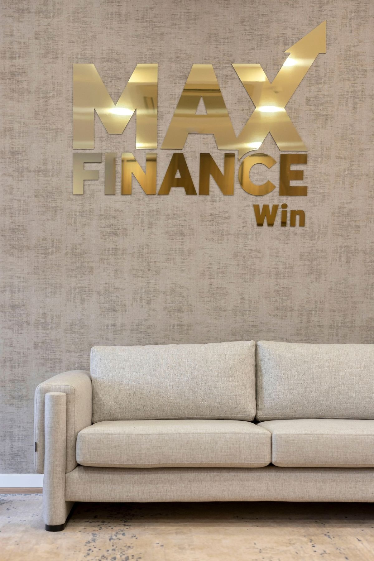 Plano aproximado do sofá em tecido alinhado cru posicionado sob o logotipo dourado da Max Finance Win no papel de parede bege.