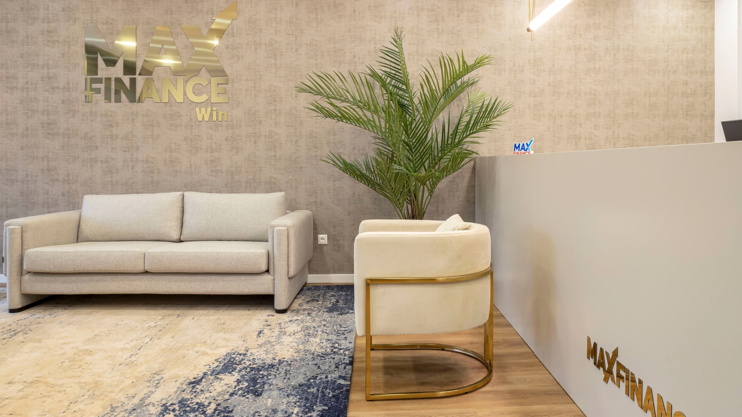 Detalhe do balcão de receção e da cadeira club em veludo com pés em aço inoxidável dourado na entrada da Imobiliária Max Finance Win.