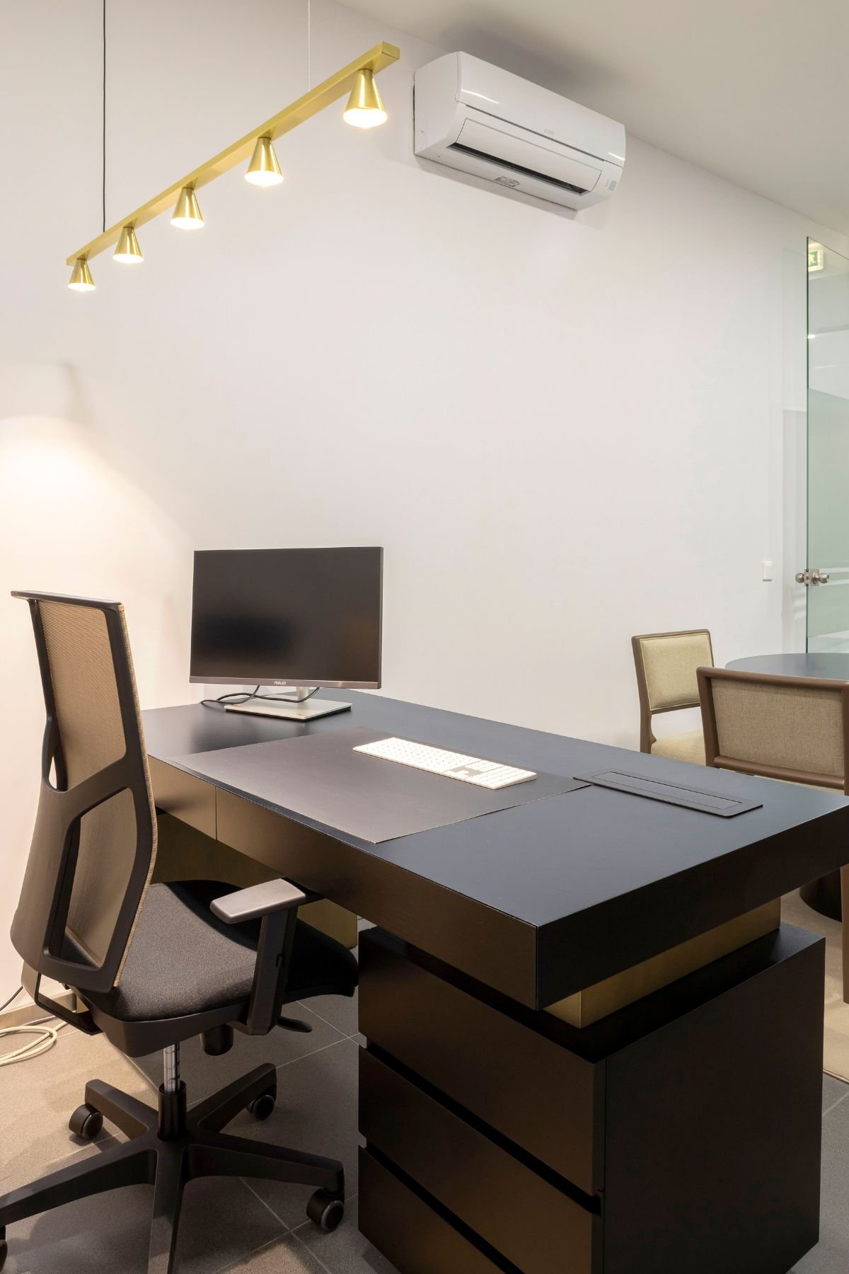 Detalhe da secretária em carvalho escurecido com base em tom bronze e candeeiro suspenso de iluminação focada no gabinete da administração da Max Finance Win.