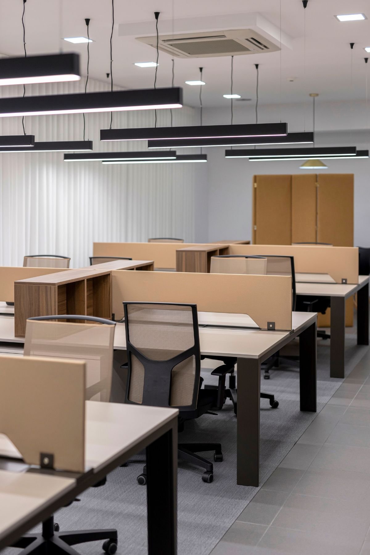 Perspetiva longitudinal do open space, realçando o alinhamento das secretárias, os divisores de secretária neutros, as cadeiras ergonómicas e a iluminação técnica suspensa.