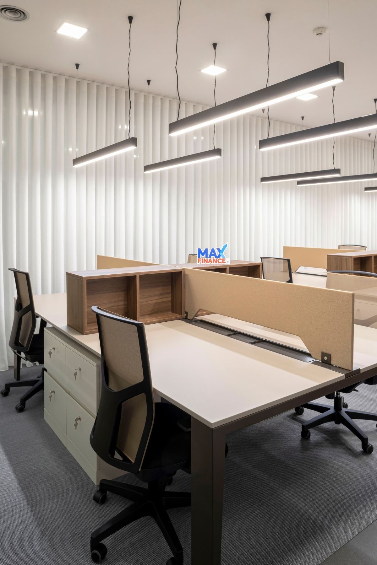 Vista em perspetiva das bancadas de trabalho partilhadas, com módulos de arrumação em madeira, divisórias estofadas em bege e cadeiras de escritório pretas.