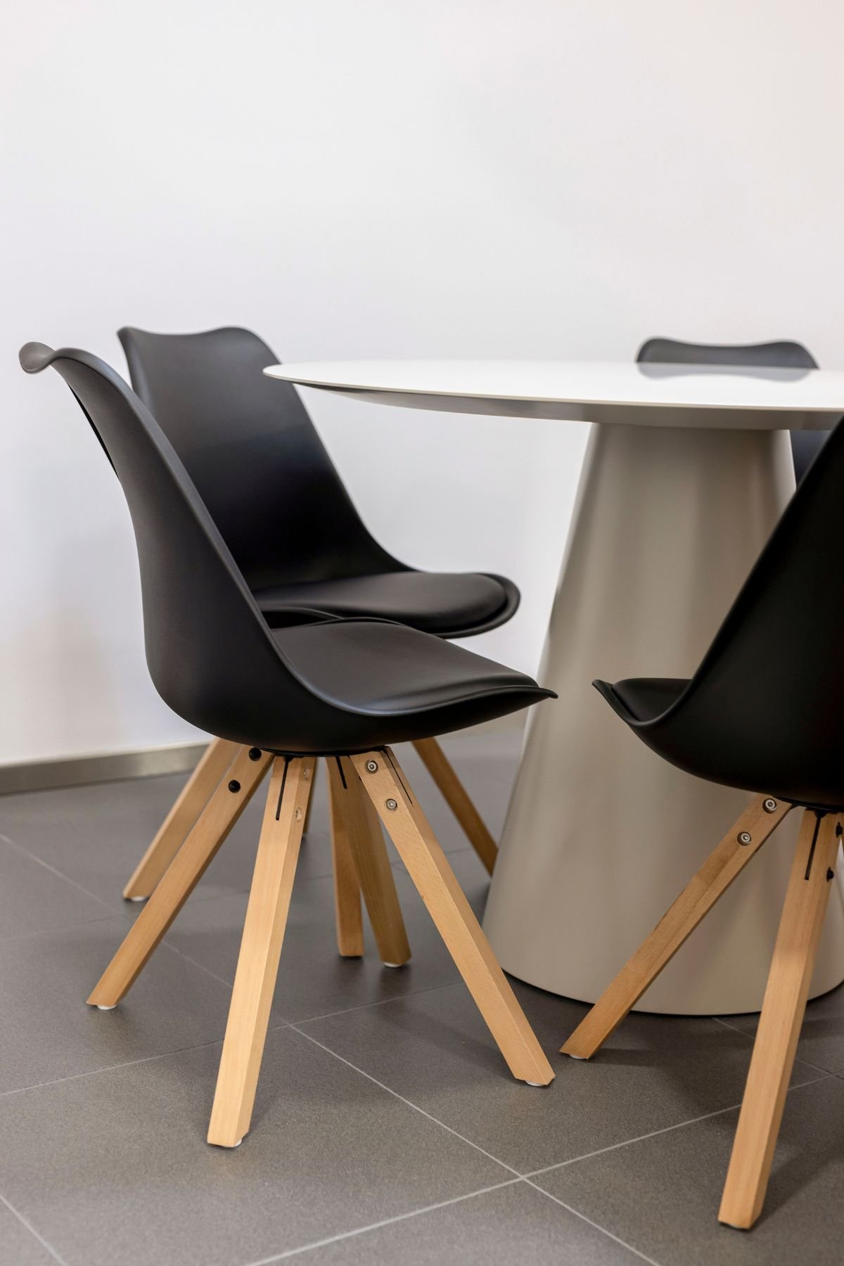 Plano aproximado das cadeiras pretas com pernas de madeira em estilo escandinavo, em torno da mesa redonda de apoio para reuniões rápidas.