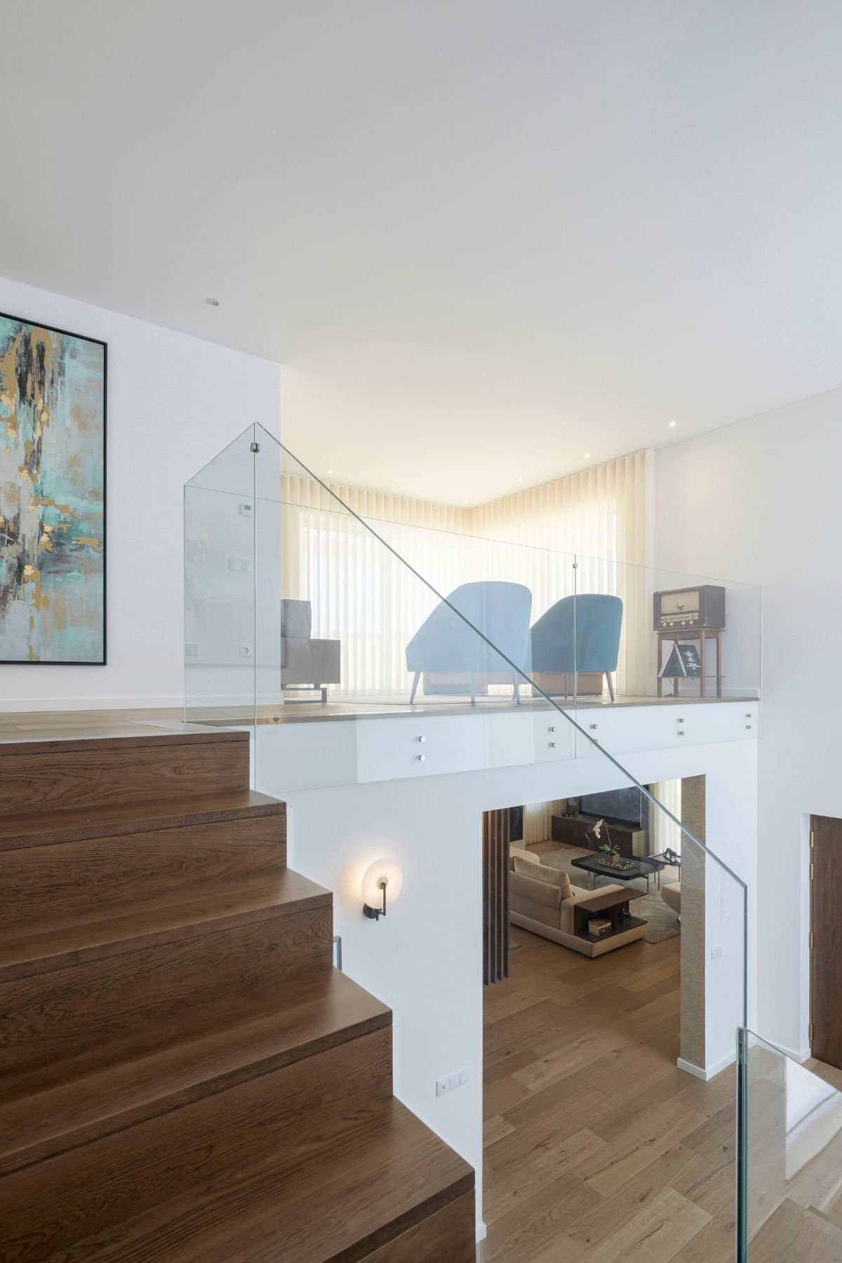 Perspetiva a partir do patamar da escada revelando a mezzanine com poltronas aveludadas e a vista para a sala de estar no piso inferior.