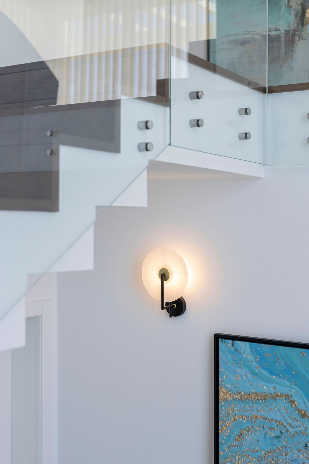 Pormenor de encanto do candeeiro de parede de design com luz quente instalado junto à estrutura da escada e ao quadro decorativo.