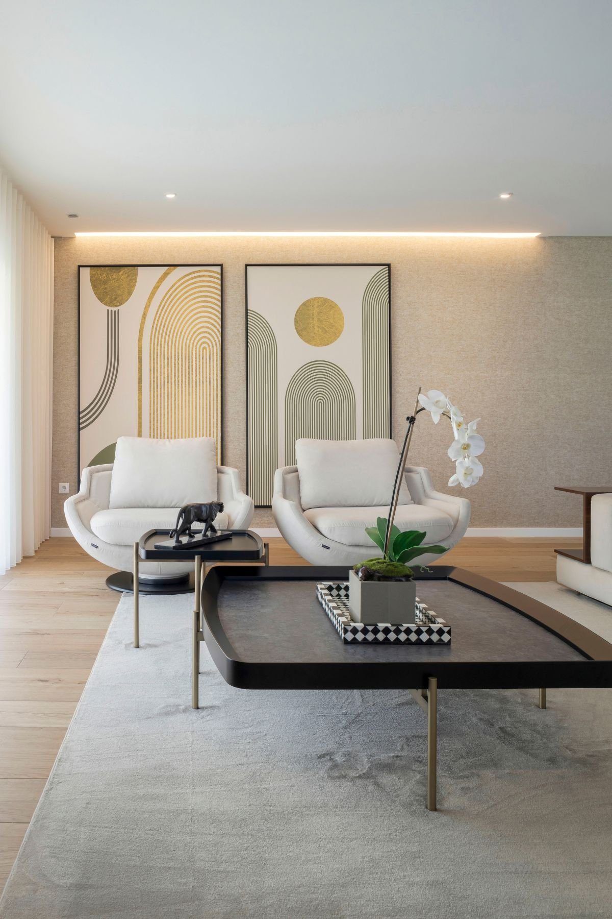 Vista frontal da zona de leitura com cadeirões aveludados, mesa de centro Capri e quadros decorativos na parede.