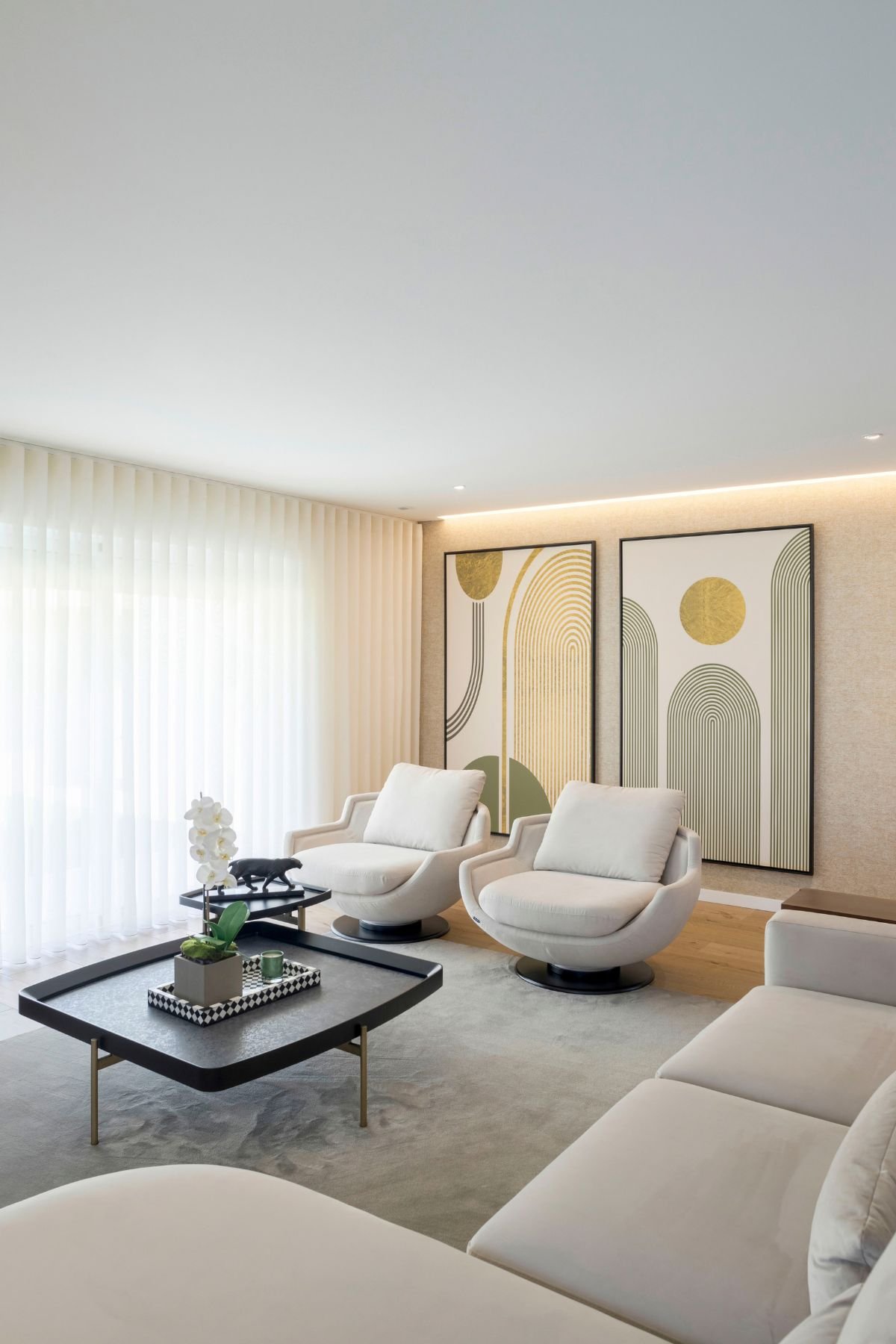 Ângulo amplo da sala de estar ressaltando a mesa de centro quadrada com arranjo floral, os cadeirões e o sofá ao fundo.