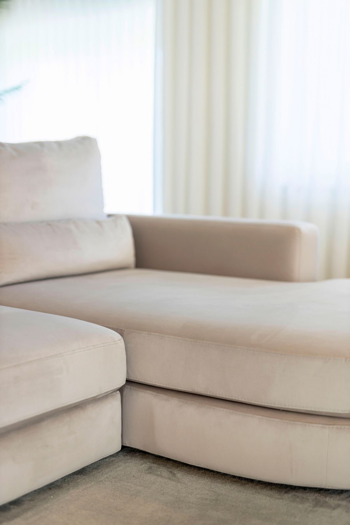Textura e pormenor do sofá com chaise longue em tecido aveludado macio junto às cortinas em tons neutros.