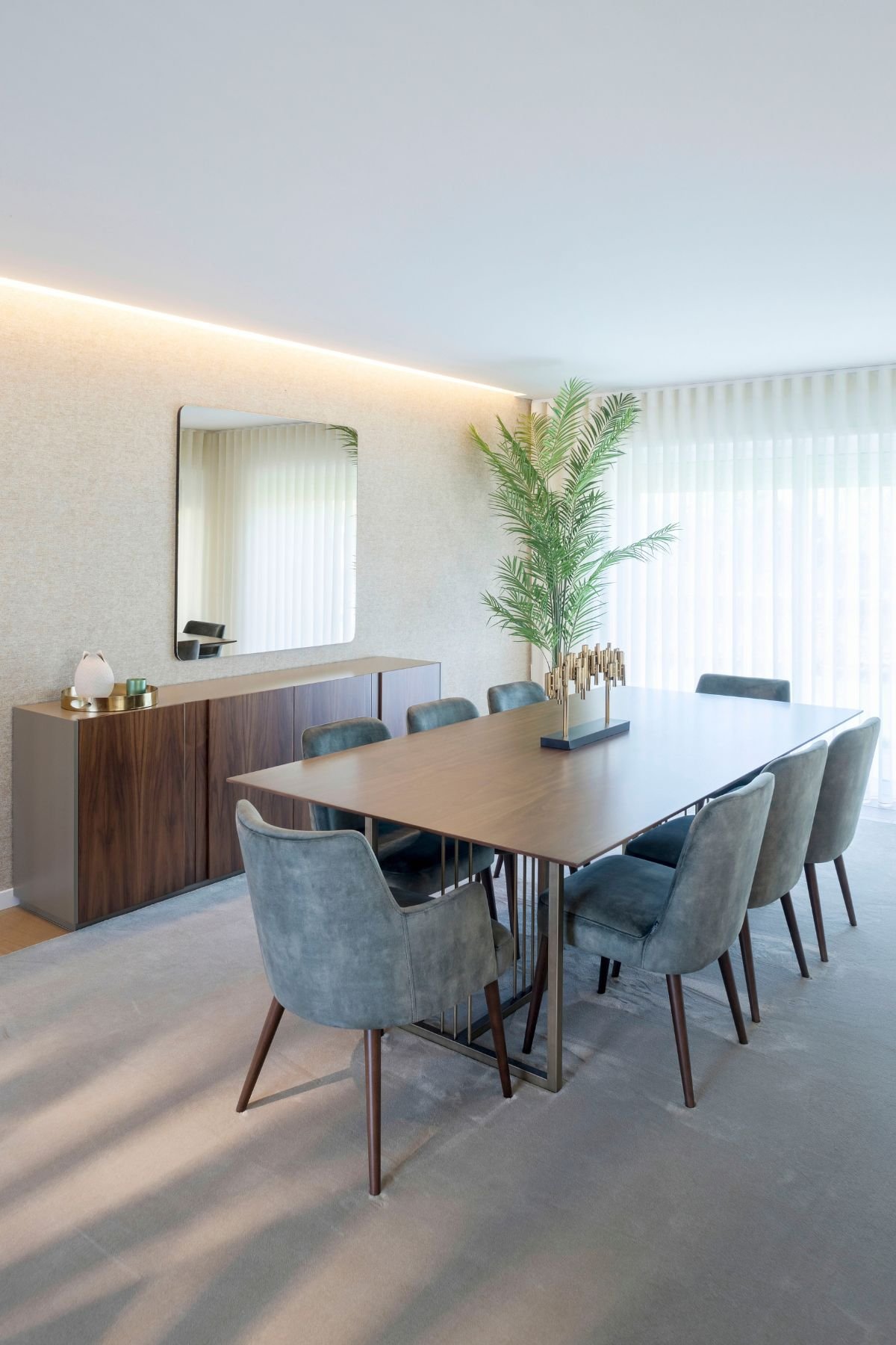 Plano vertical em ângulo da mesa de jantar acompanhada pelas cadeiras de veludo e iluminação sutil.