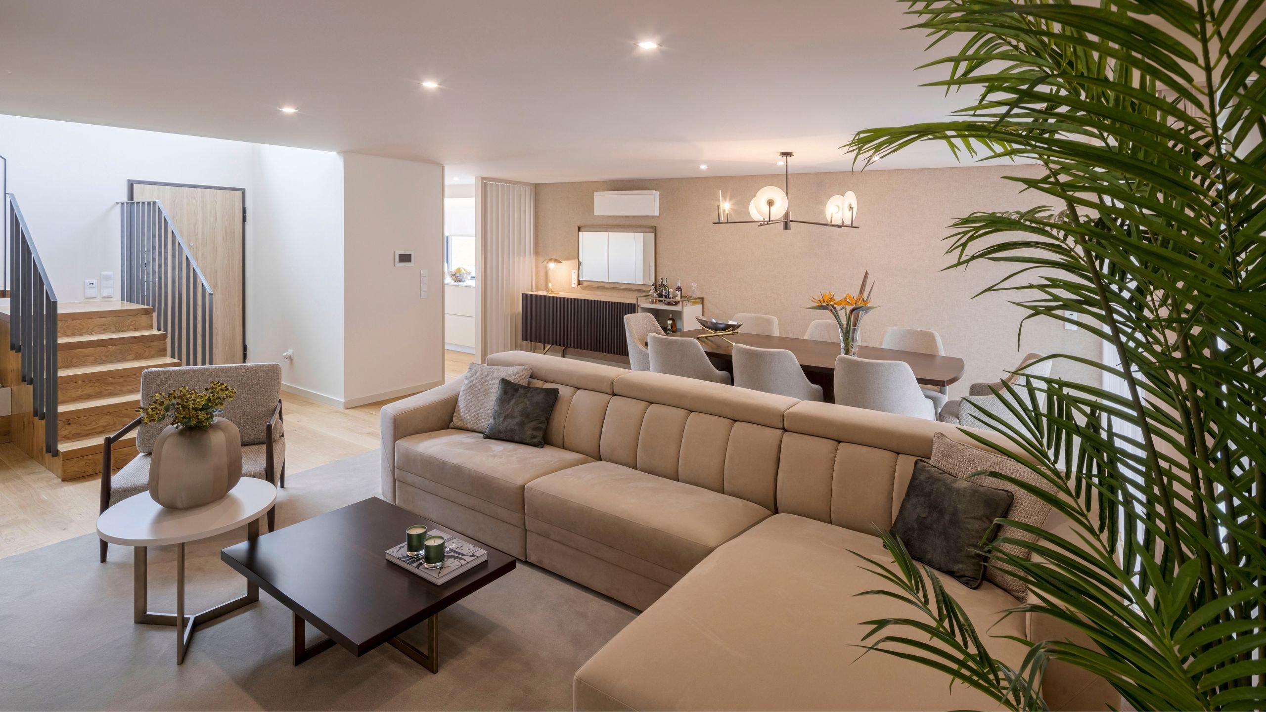 Panorâmica de sala ampla com zona de estar e jantar em open space ladeada por vegetação, demonstrando a grandiosidade de interior design e decoração em casas de luxo.
