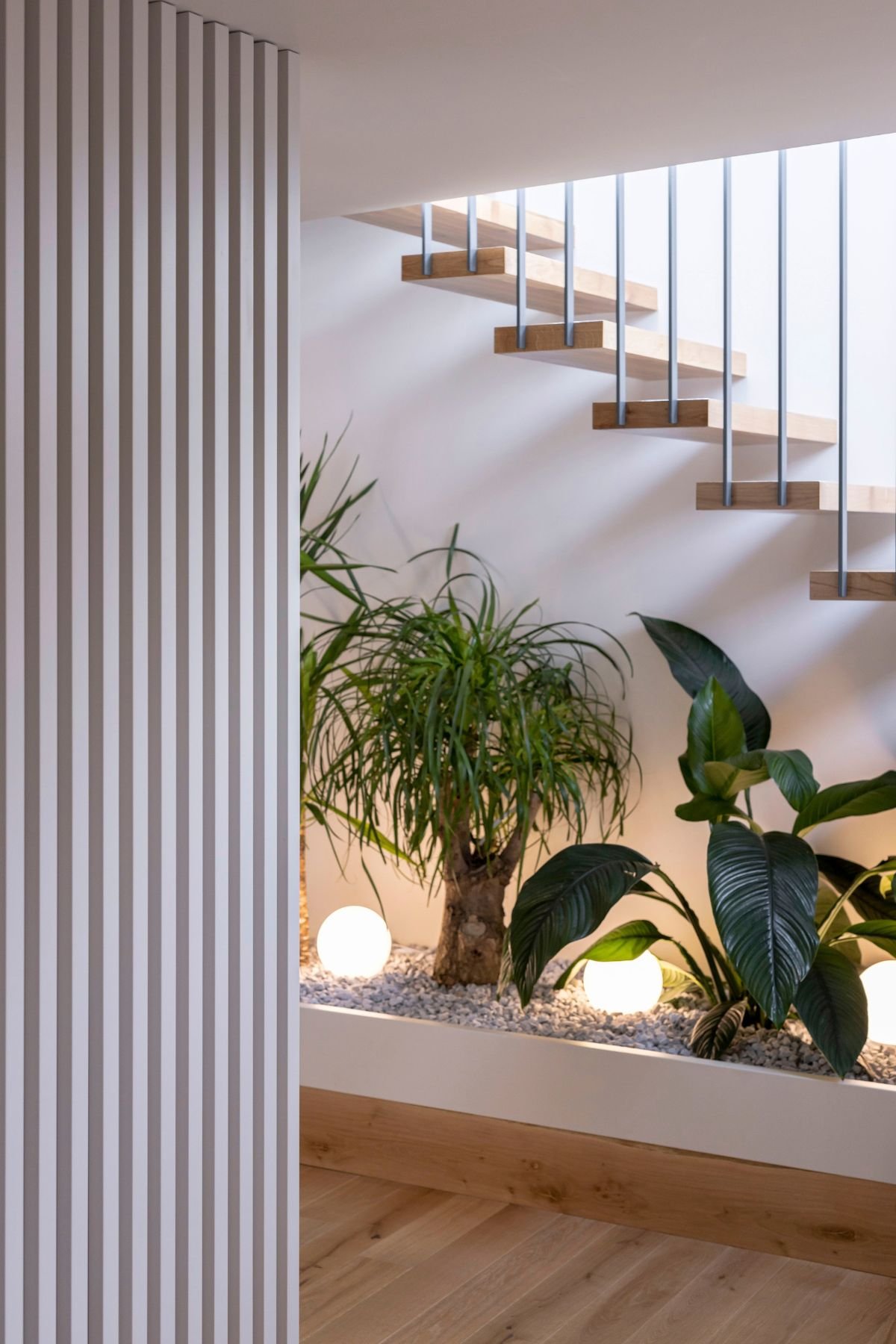 Pormenor de jardim interior iluminado sob escadaria moderna em open space com ripado elegante, unindo nobre interior design e decoração para casas de luxo.