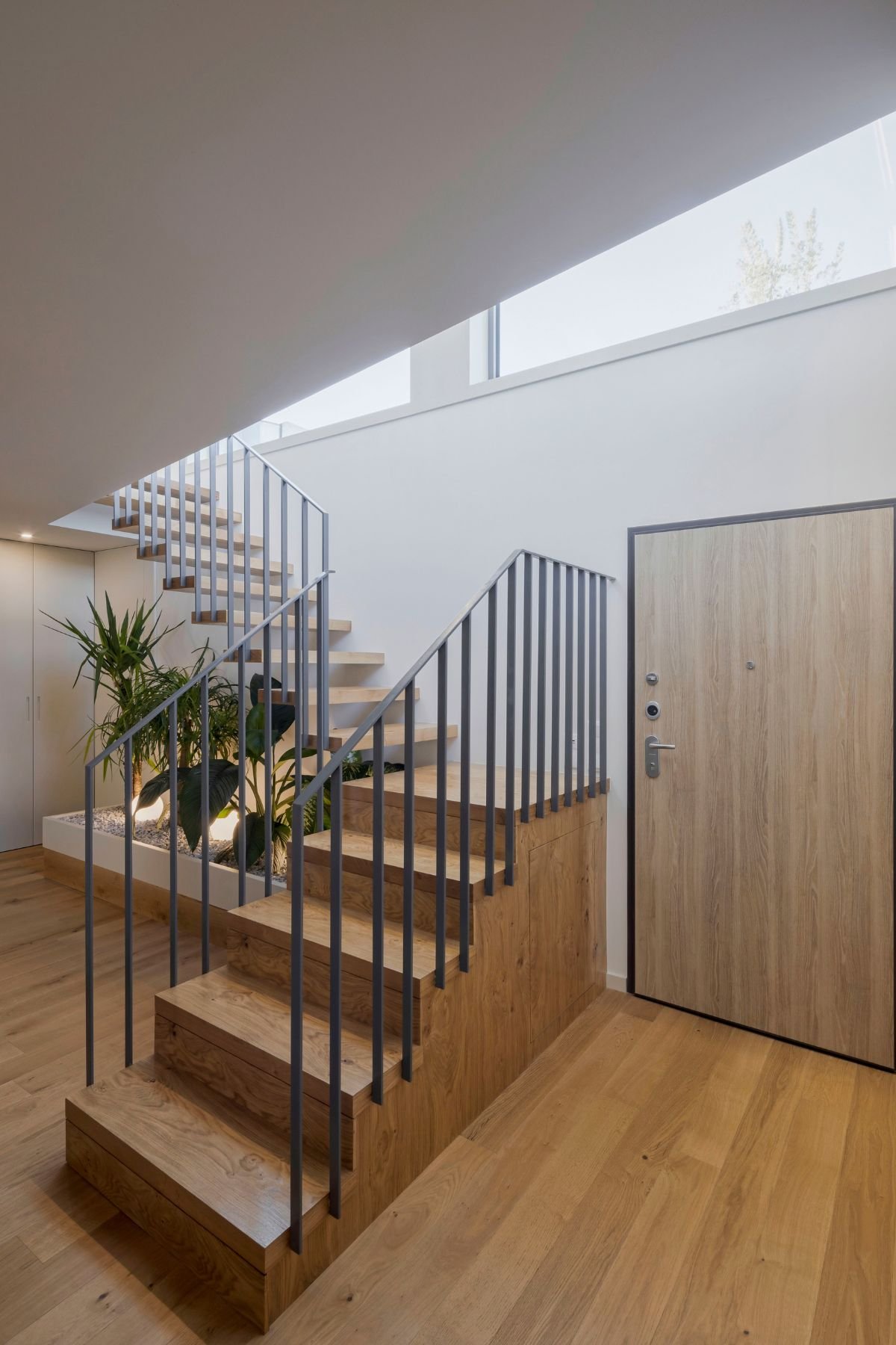 Escada suspensa em madeira com jardim interior sob os degraus em open space, refletindo o requinte de interior design e decoração em casas de luxo.
