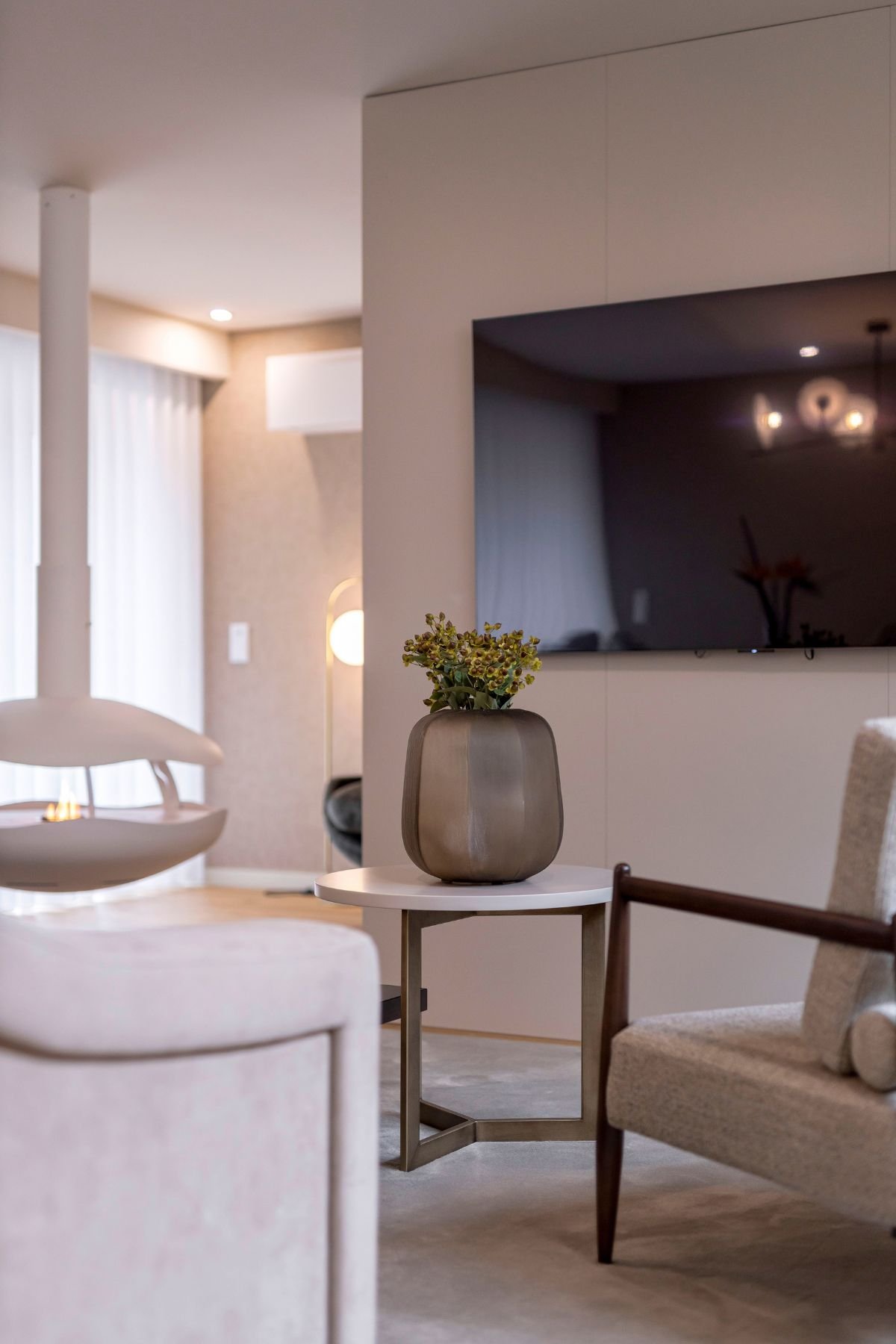 Mesa de apoio com jarra decorativa e poltrona em open space sofisticado com lareira suspensa, expressando a nobreza de interior design e decoração em casas de luxo.