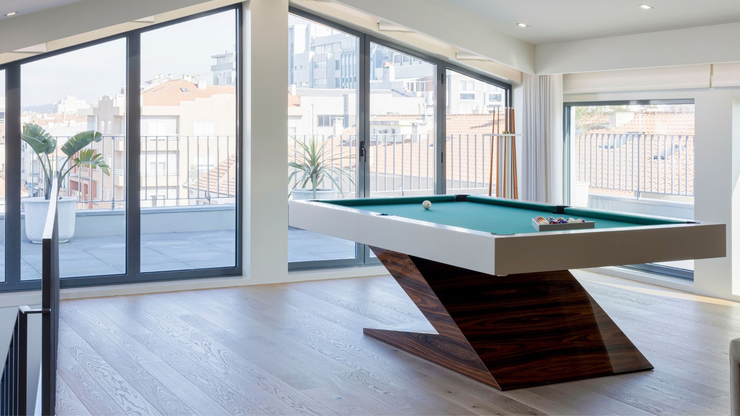 Mesa de bilhar escultural em open space luminoso com grandes janelas, integrando na perfeição o projeto de interior design e decoração de salas de estar modernas.