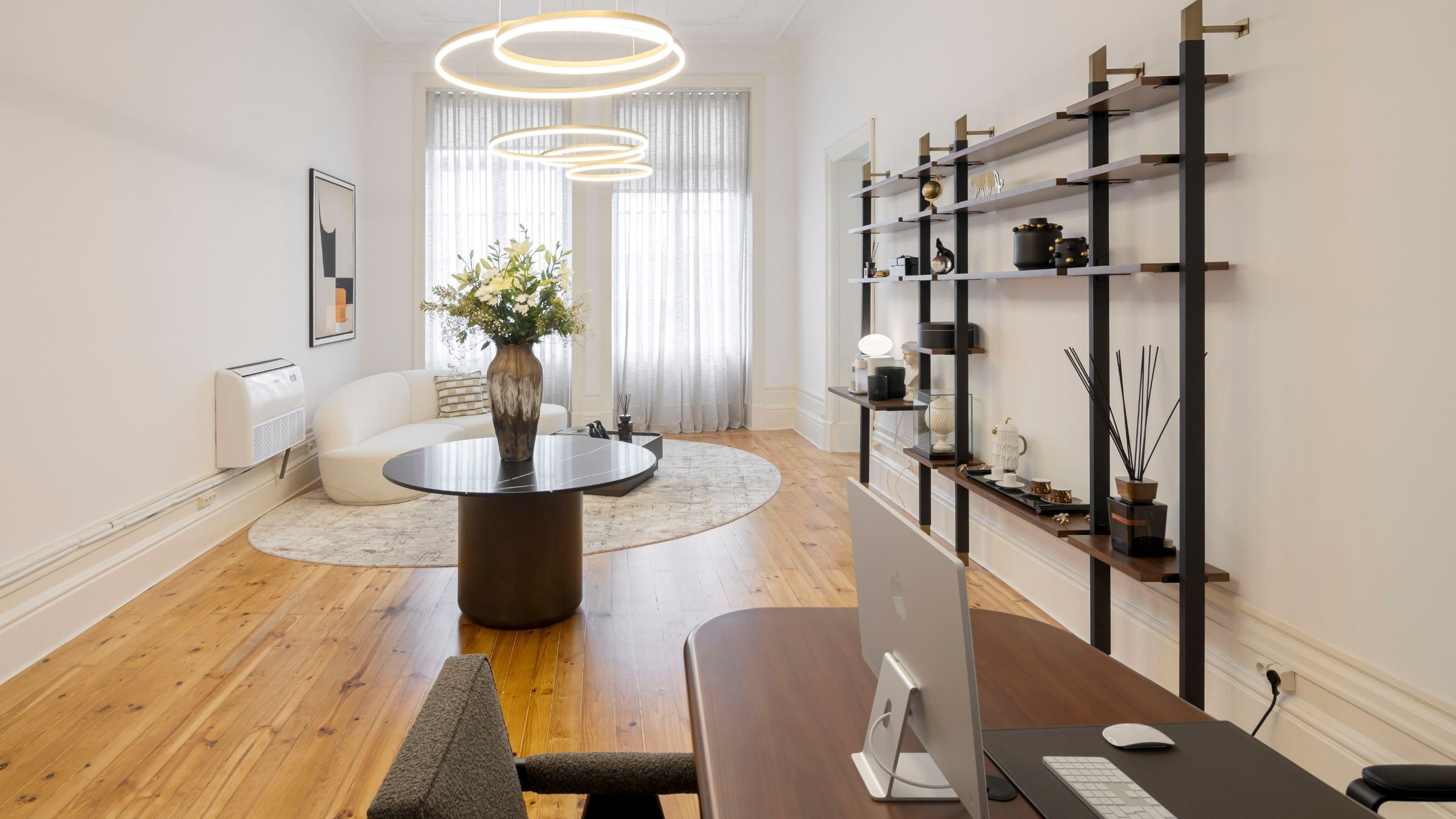 Receção moderna com sofá curvo claro, estante metálica de parede e candeeiros de teto circulares para uma decoração sala moderna.