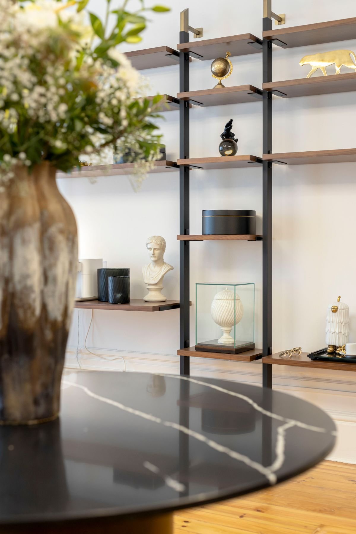Mesa de centro em mármore com vasos decorativos em primeiro plano e estante modular com artigos de decoração ao fundo.