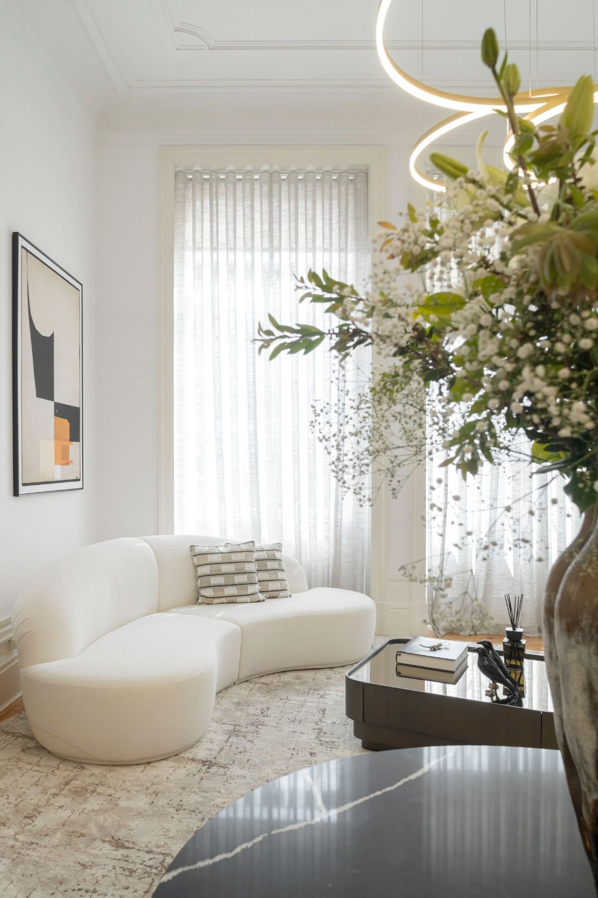 Sofá branco de linhas orgânicas e mesa de centro espelhada com jarra flores em destaque, ideais para a decoração sala moderna.