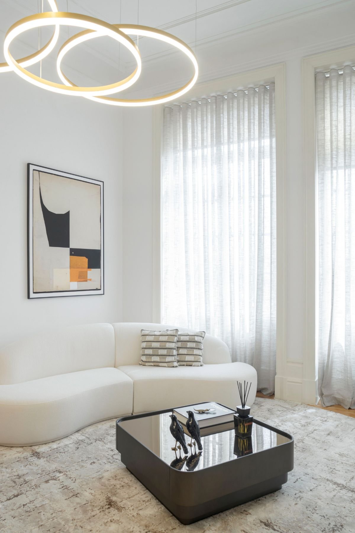 Sofá curvo branco acompanhado por mesa de centro sala escura e quadros decorativos na parede, criando um ambiente de sala de estar aconchegante.