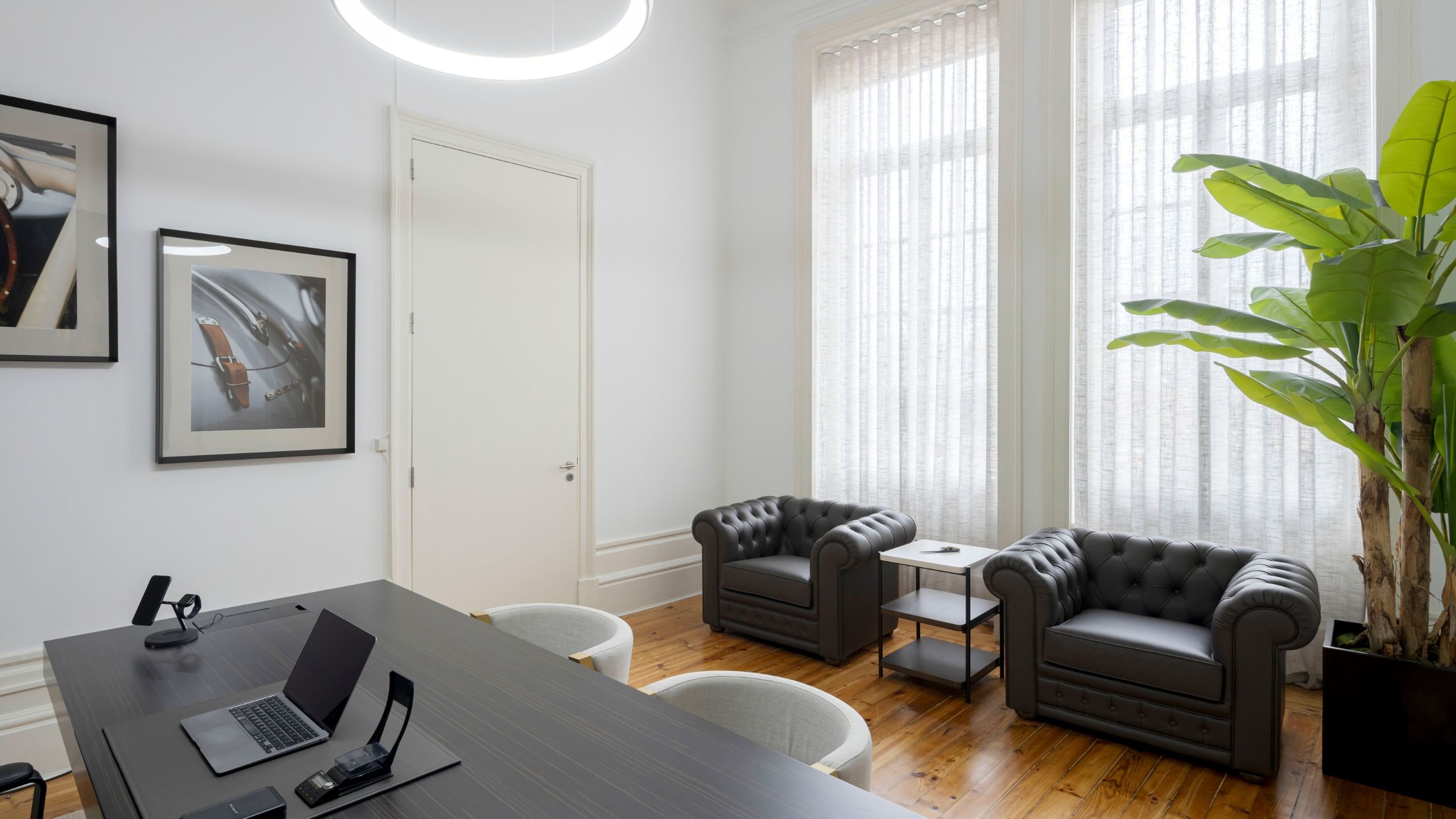 Gabinete de trabalho com secretária, cadeiras de escritório, cadeirões de pele e planta decorativa num projeto de interiores executivo.