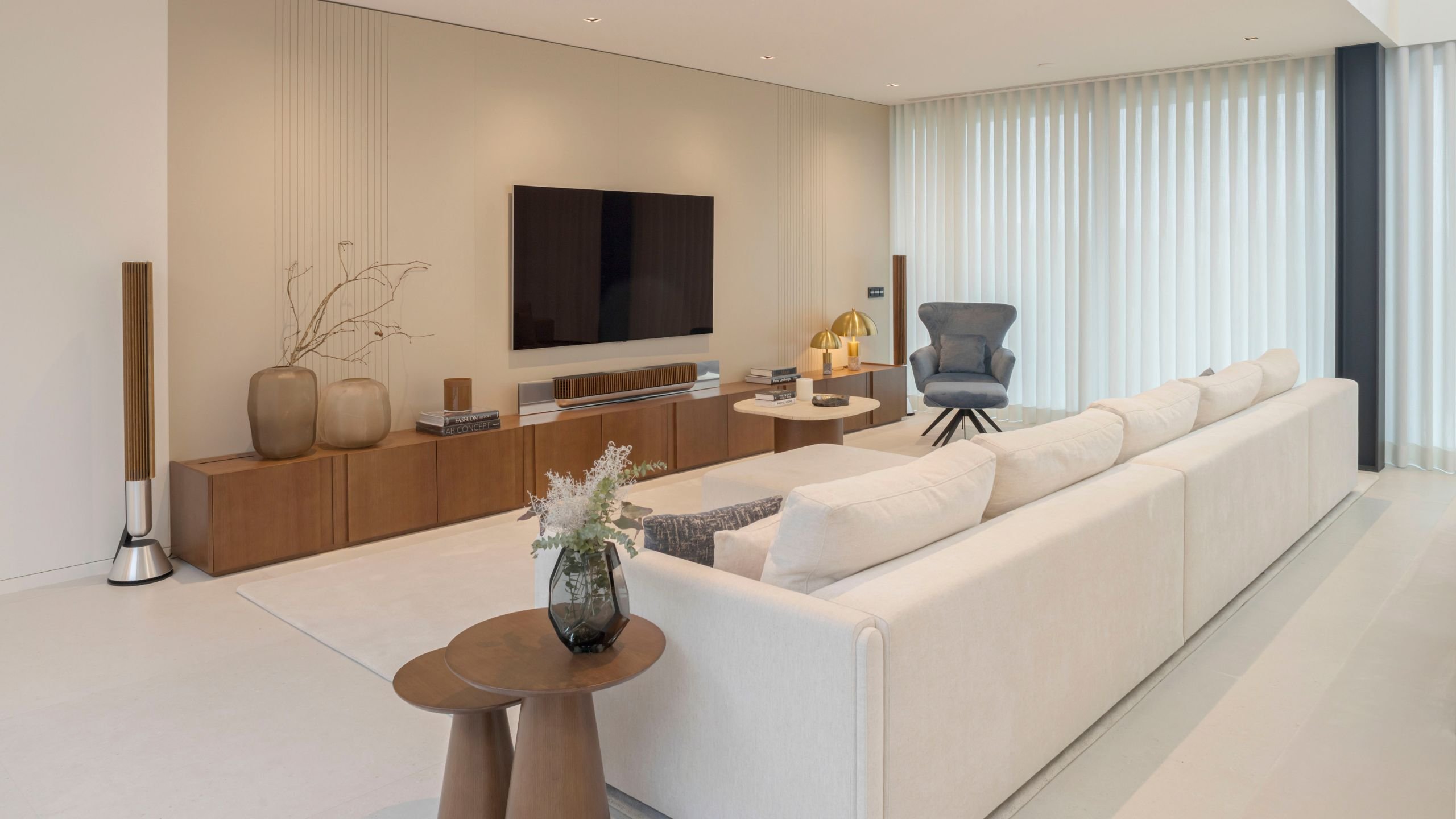 Sala de estar moderna com sofá em tom claro, móvel tv em madeira, mesa de apoio e cadeirão azul num projeto de interiores.