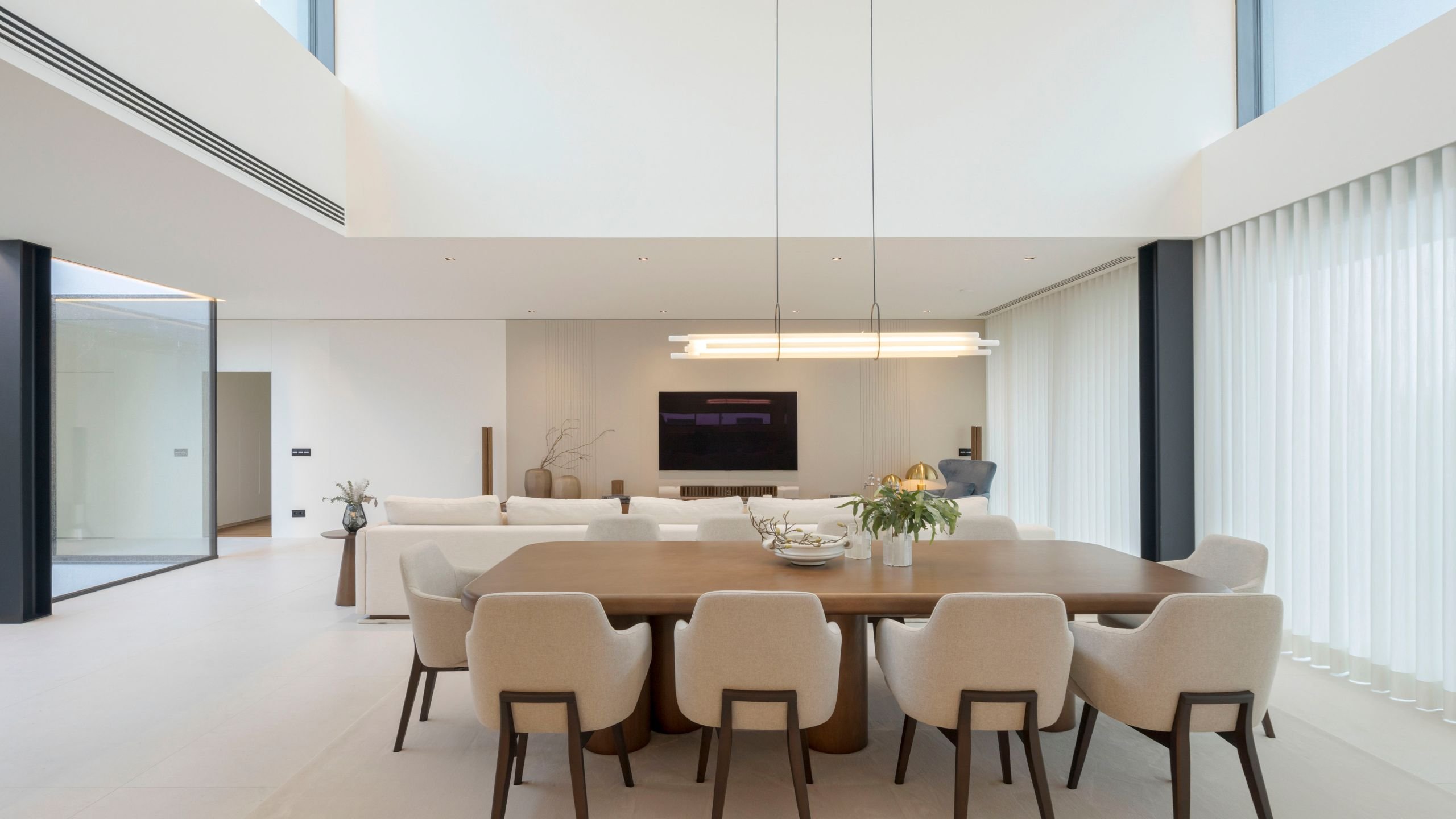 Sala de jantar integrada com sala de estar moderna em open space, destacando grande mesa de jantar em madeira e cadeiras de jantar estofadas.