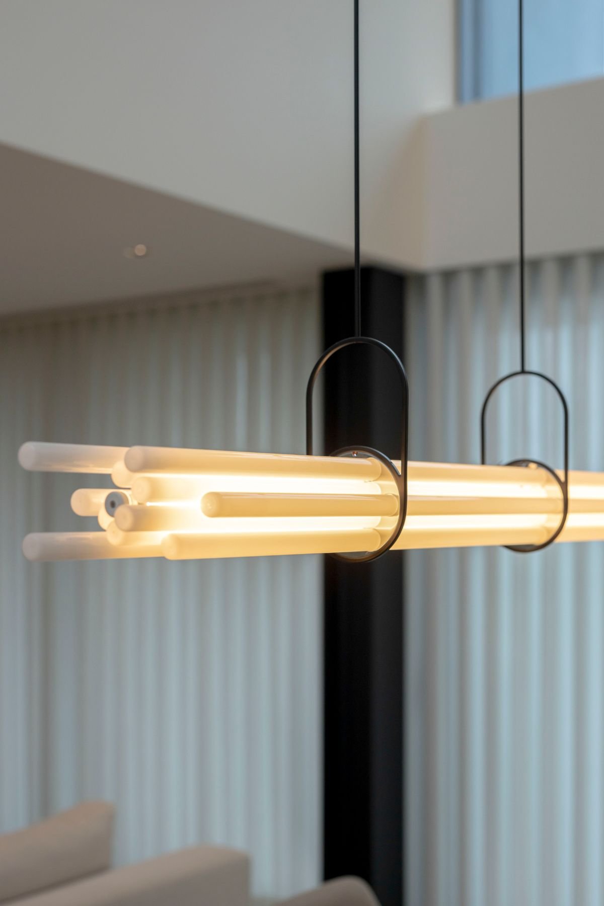 Candeeiro de teto moderno com design tubular e luz quente suspenso sobre a zona de refeições.