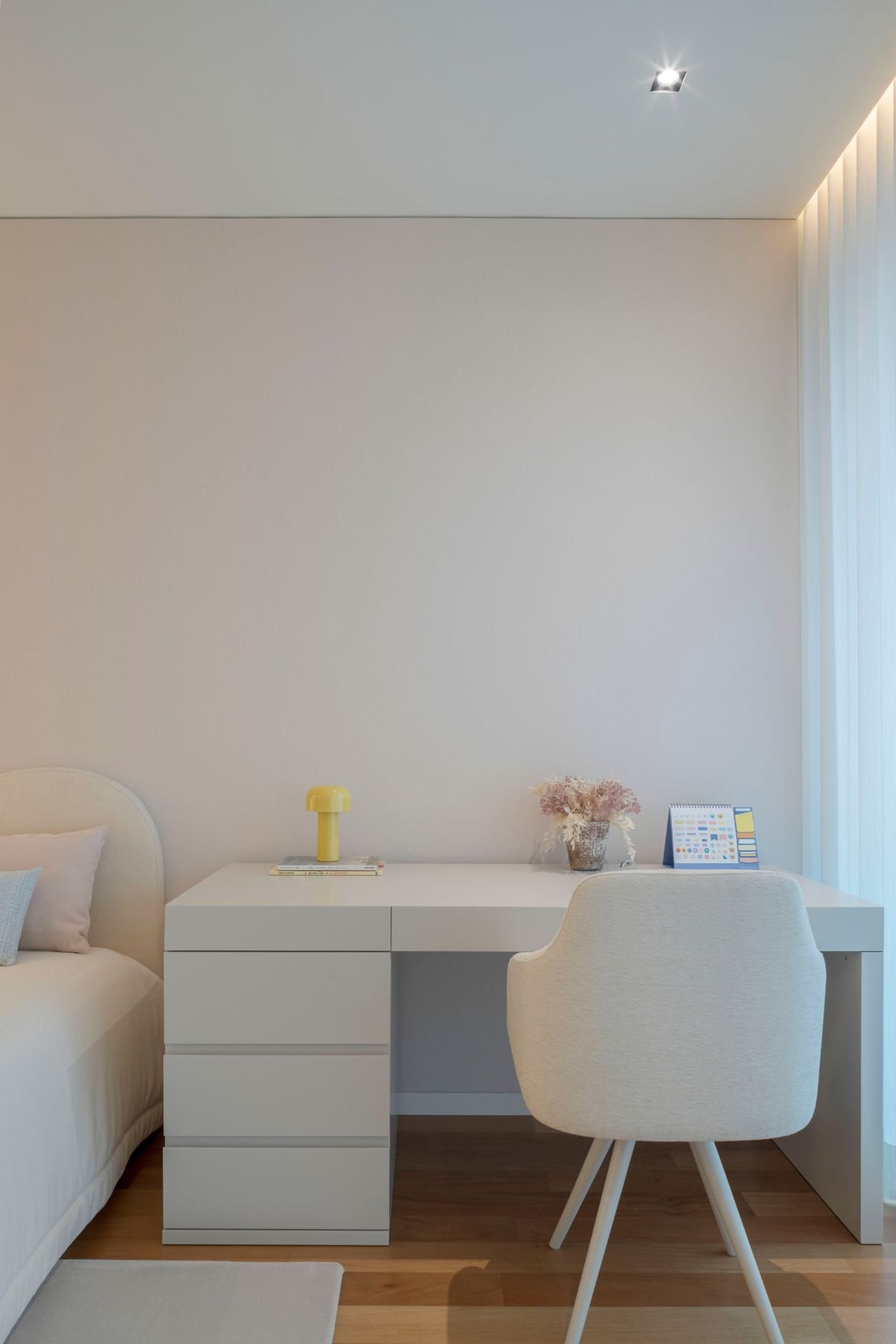 Secretária de trabalho branca com cadeira de escritório estofada em ambiente minimalista de quarto juvenil.