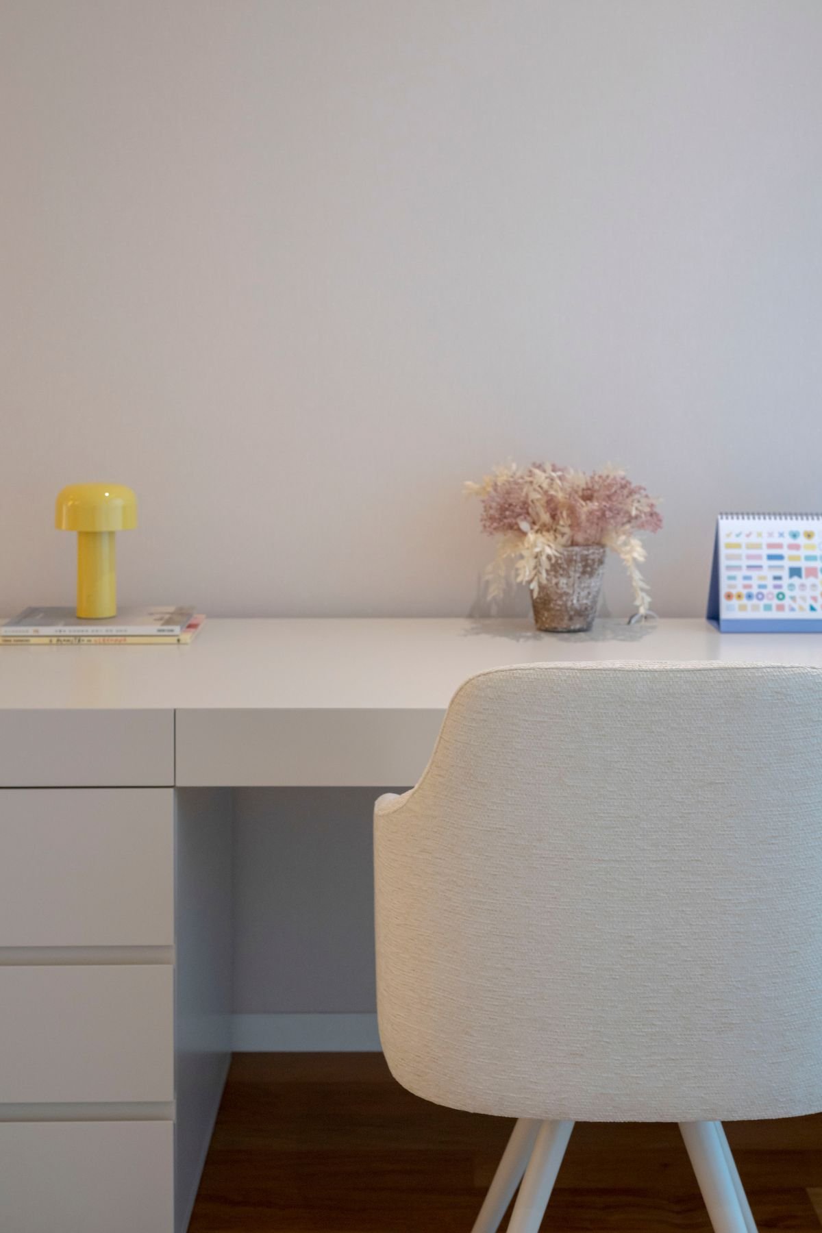 Pormenor da secretária com cadeira de escritório em tecido e pequeno candeeiro de mesa amarelo decorativo.