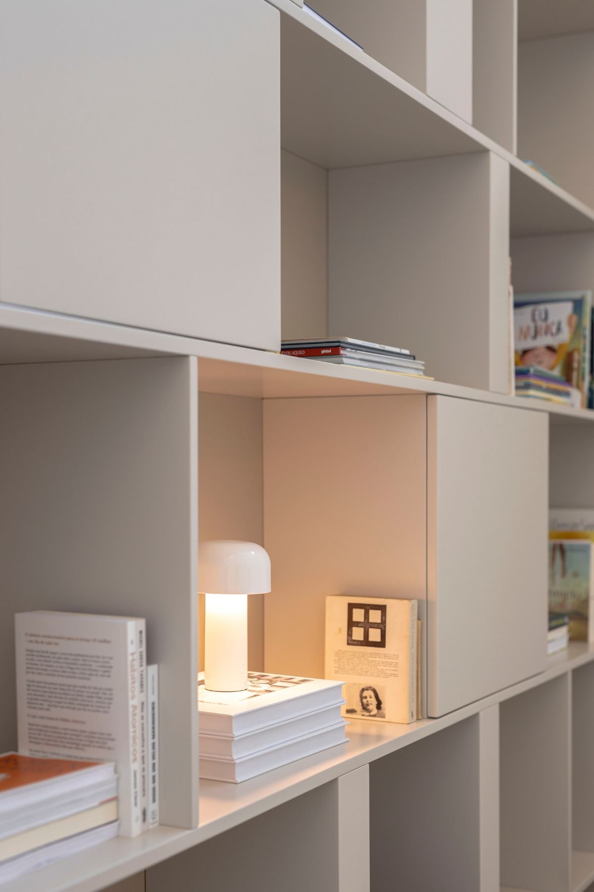 Pormenor do nicho da estante de livros com candeeiro de mesa minimalista aceso e livros decorativos no escritório.