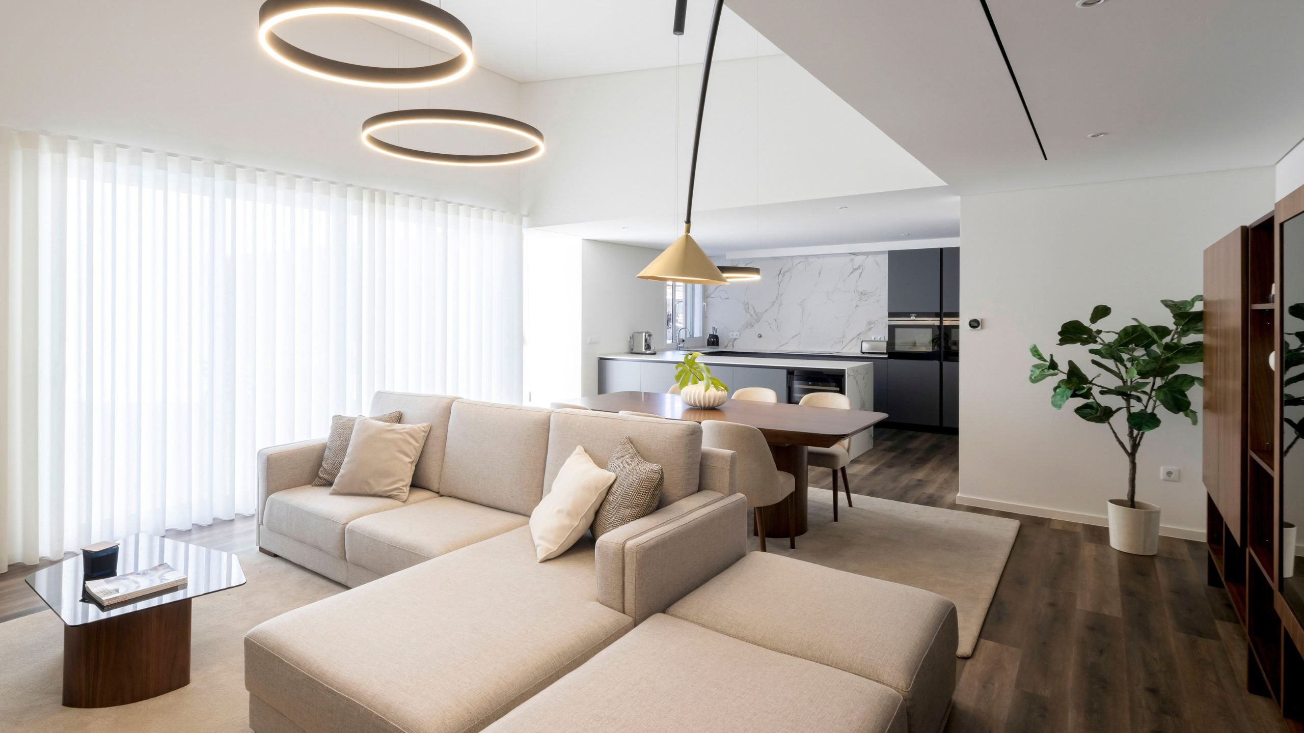 Panorâmica da sala de estar moderna e luminosa com sofá chaiselongue e mesa de jantar em madeira de nogueira.