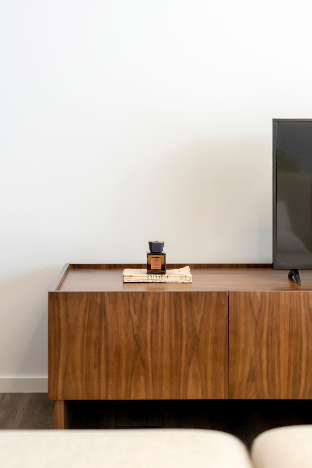 Pormenor do móvel de tv em madeira de nogueira com frasco de perfume decorativo e livros no design de interiores.
