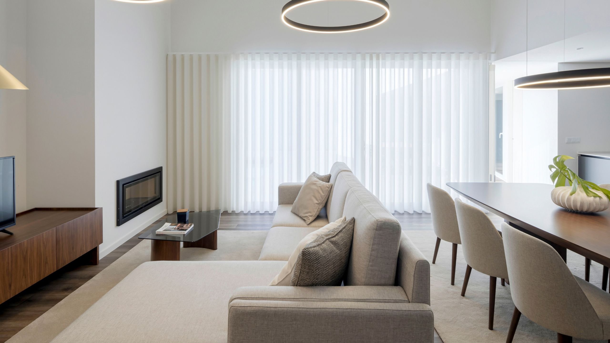Ambiente integrado de sala de estar e jantar com sofá modular em tom bege e cadeira de jantar estofada em espaço com recuperador de calor.