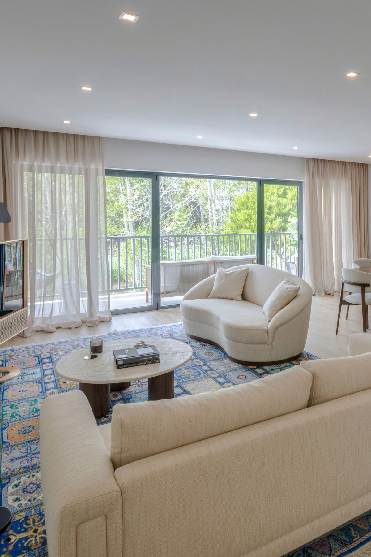 Ângulo da sala de estar focando no sofá curvo James de tom neutro, junto à janela da varanda e rodeado por elementos de design de interiores.
