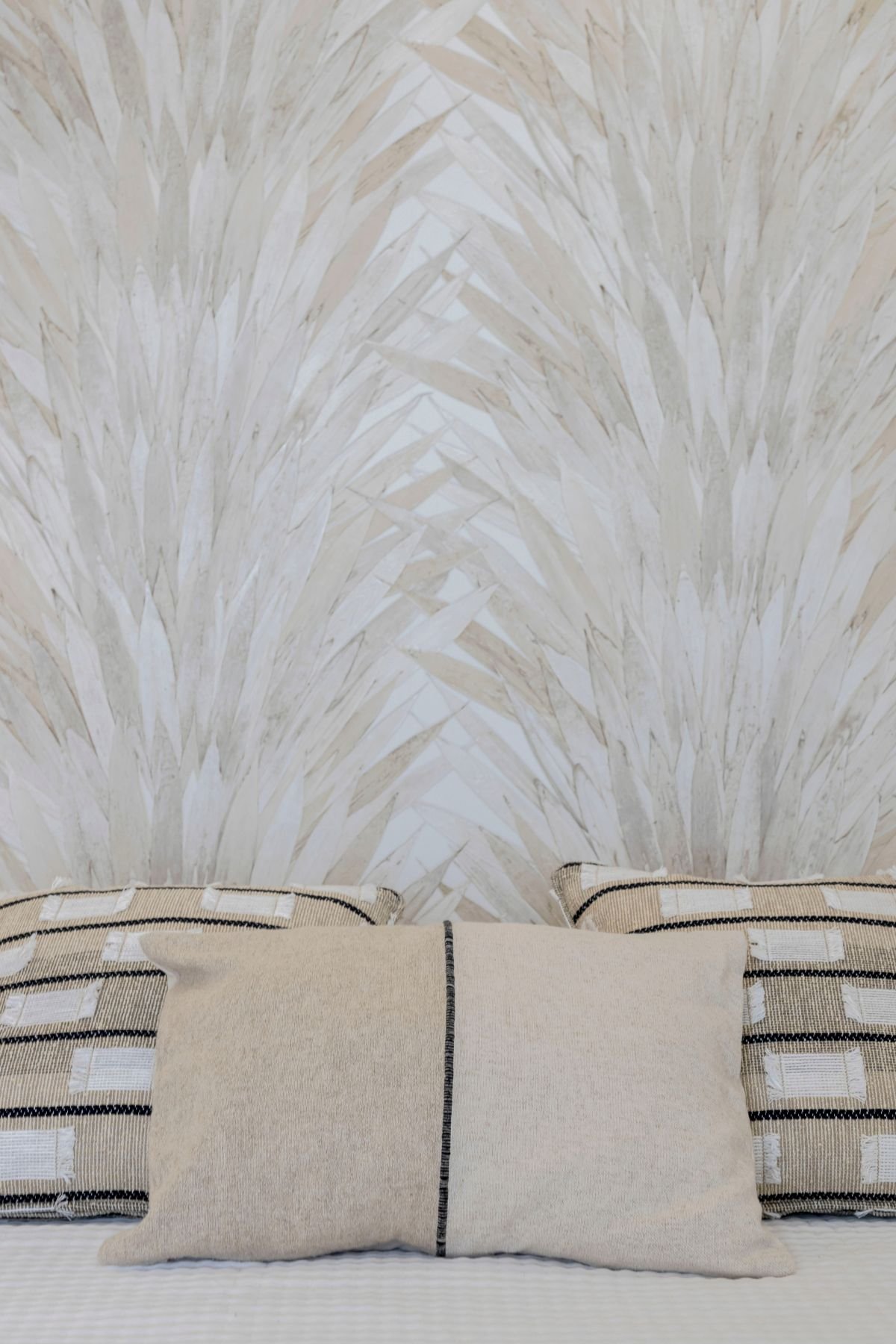 Plano aproximado das almofadas decorativas em tons neutros e padrões geométricos sobre o papel de parede de inspiração natural.