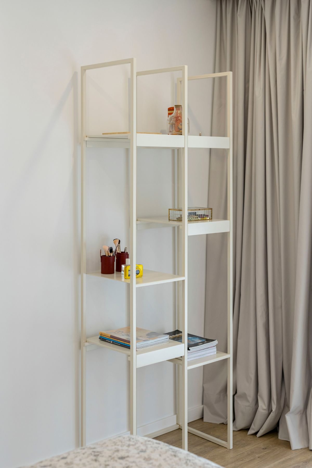 Detalhe da estante metálica branca de design leve e geométrico, decorada com livros e pequenos objetos organizadores.