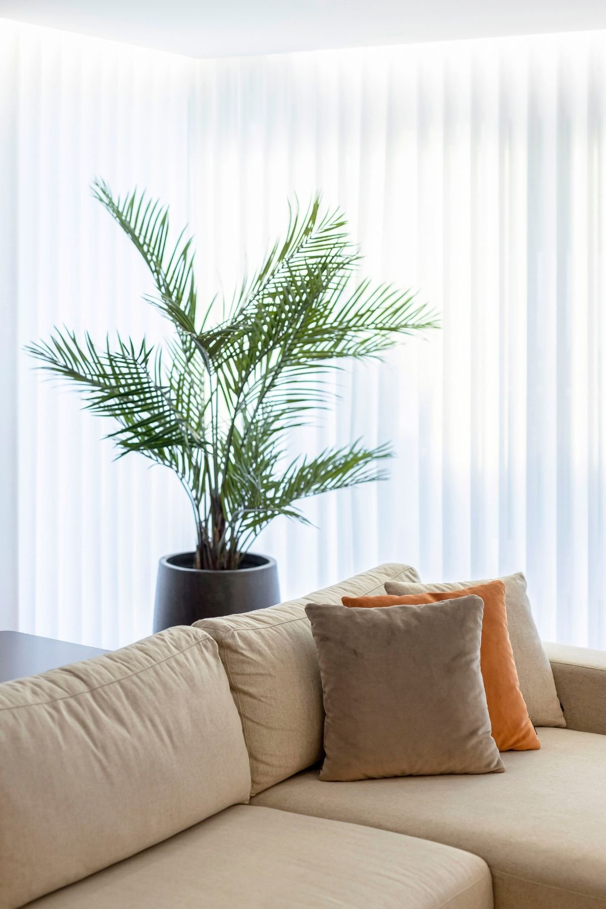 Perspetiva longitudinal da sala de estar moderna, focando nas duas poltronas giratórias creme com base dourada, no sofá de canto e no móvel de parede com televisão.