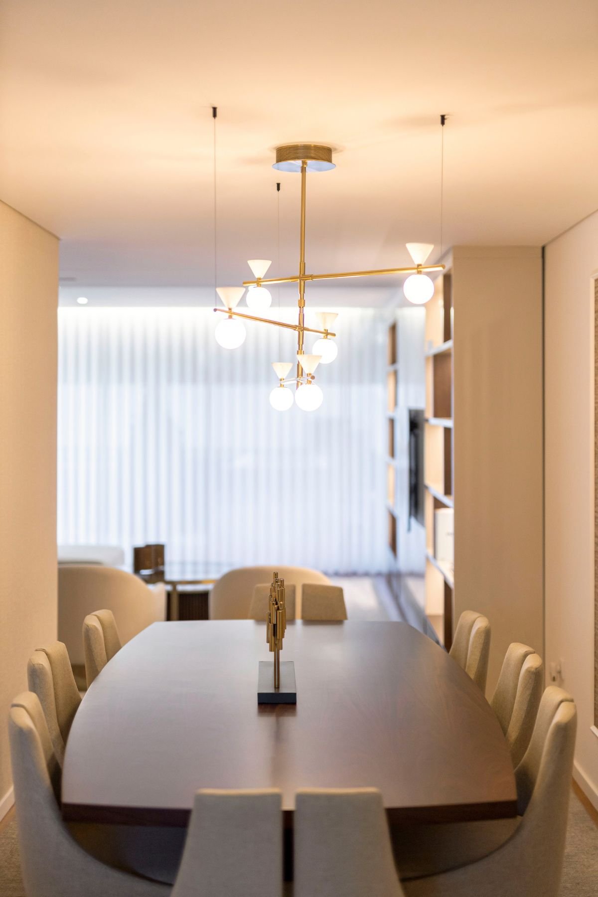Pormenor da mesa de jantar em nogueira com peça decorativa, realçando o design irreverente do candeeiro suspenso e a transparência da cortina.