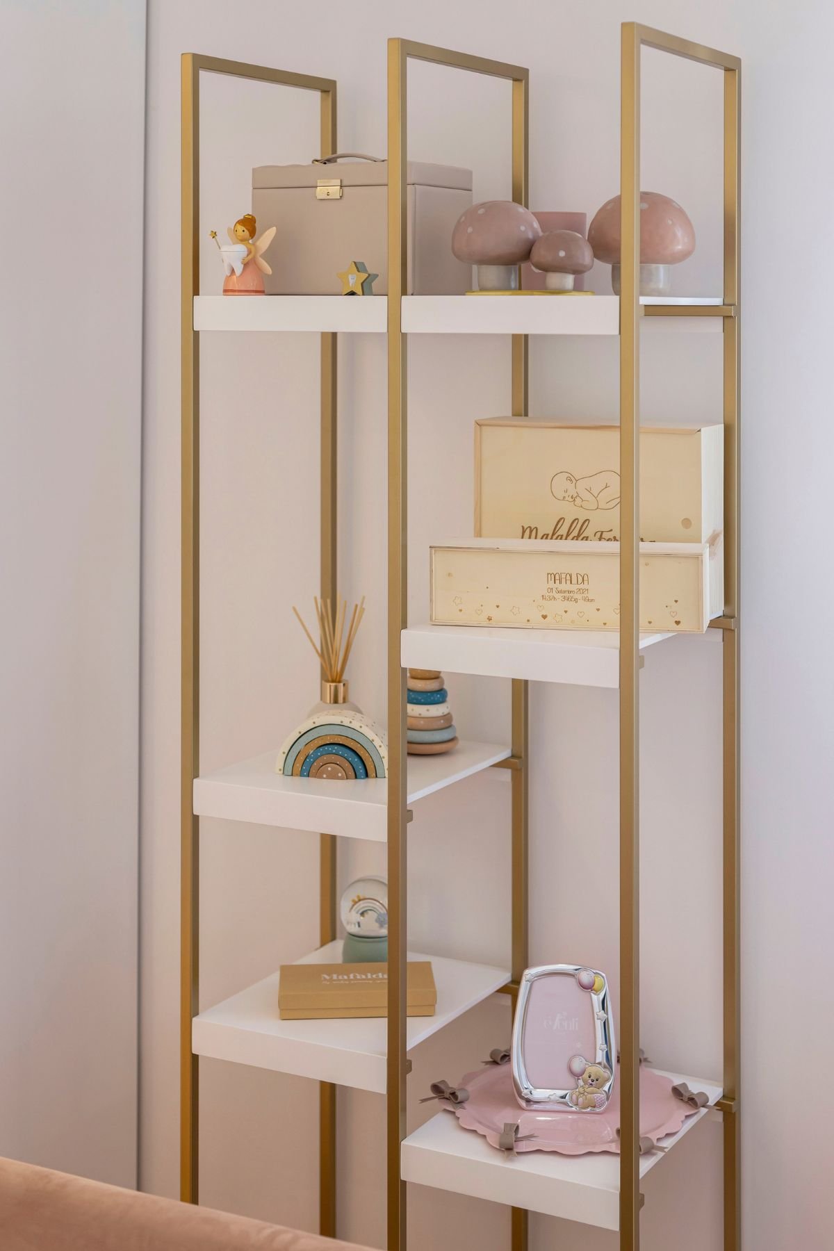 Plano aproximado das prateleiras do conjunto de estantes dourado, exibindo decorações infantis, incluindo caixas personalizadas, brinquedos de madeira e molduras.
