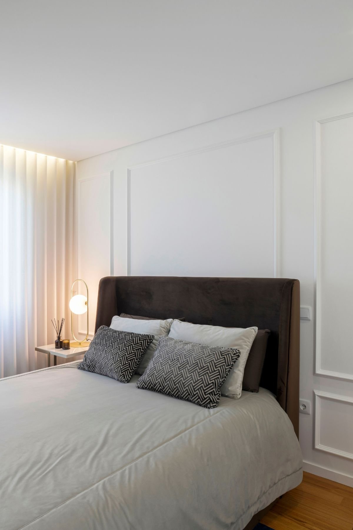 Plano detalhado da lateral da cama de hóspedes, focando nas almofadas texturizadas, na extremidade da cabeceira e na parede com relevos geométricos elegantes.