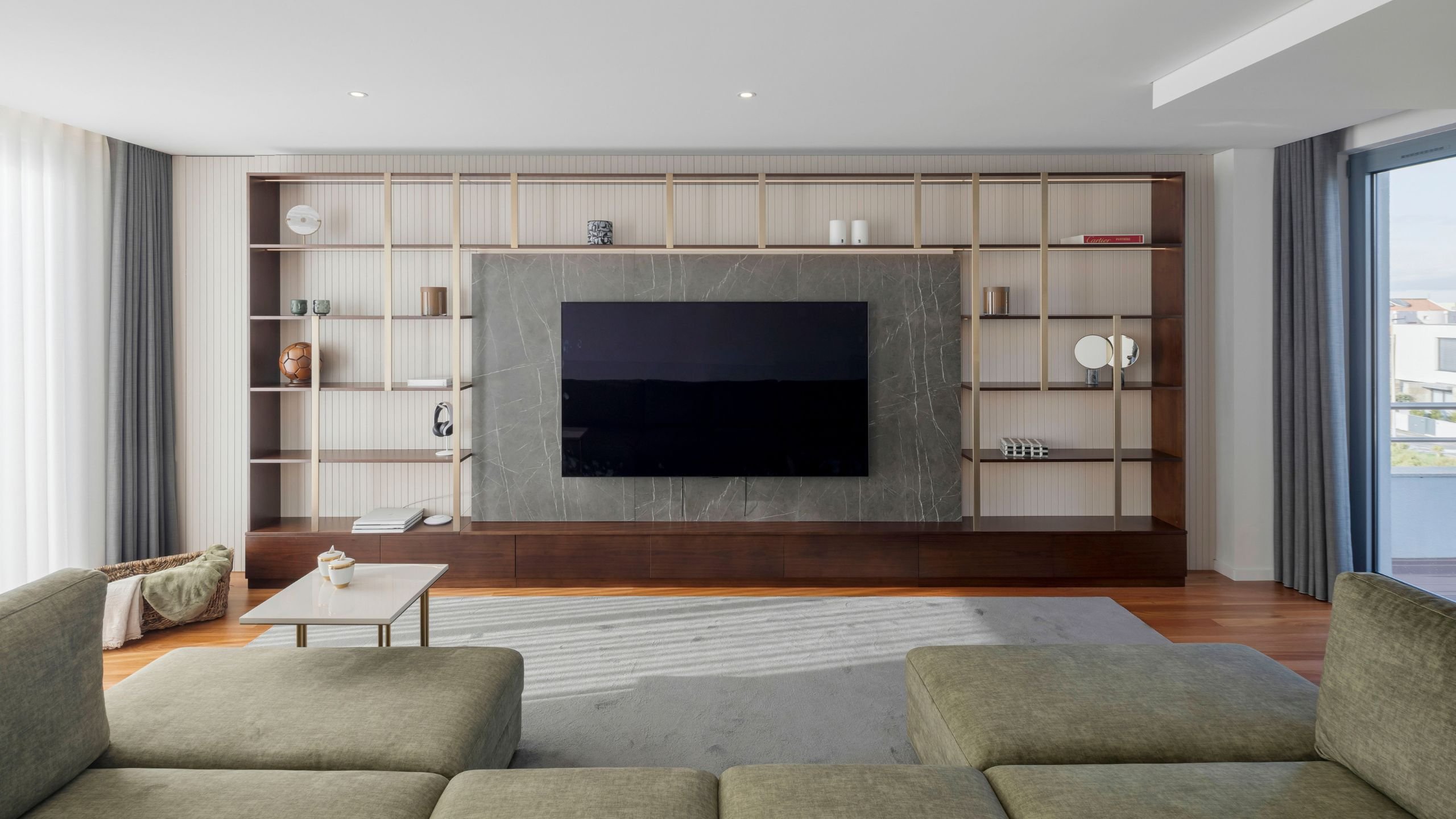 Visão frontal e centralizada do home cinema, com o grande ecrã de TV emoldurado pelo painel de cerâmica efeito mármore e pelas estantes laterais simétricas.