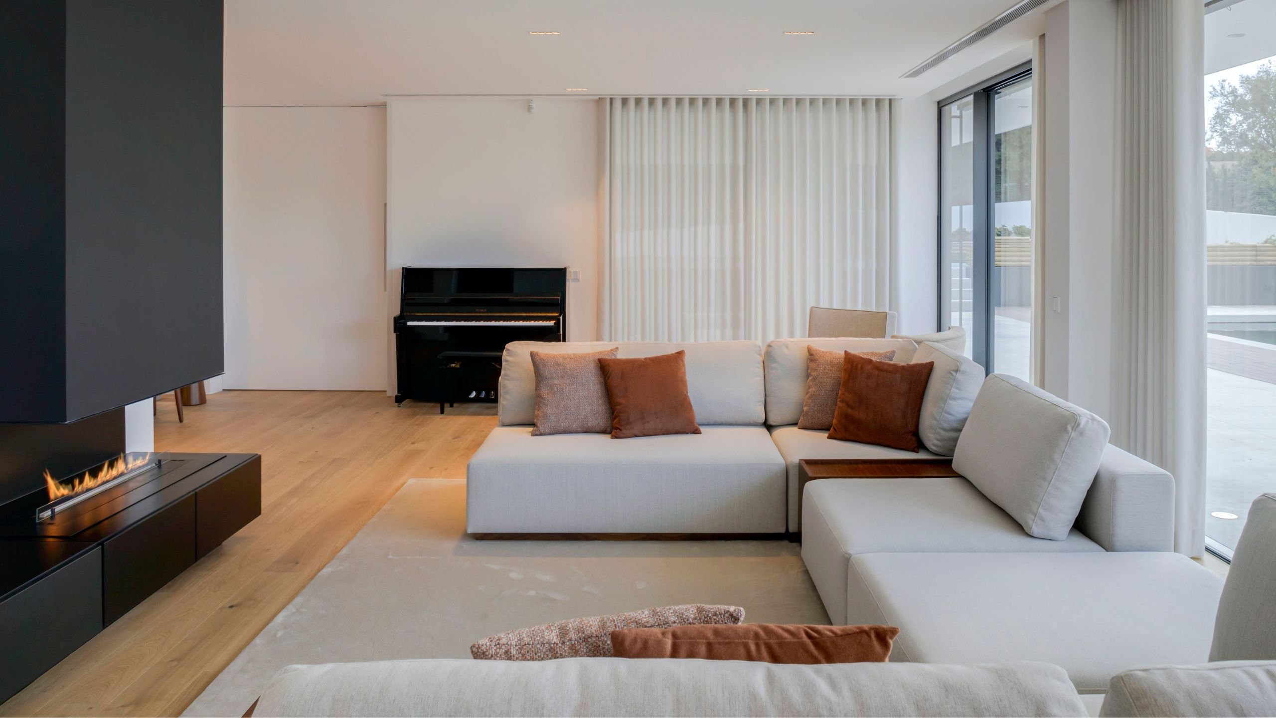 Sala de estar ampla na Moradia Oeiras com sofá modular em tom neutro, almofadas terracota, lareira moderna embutida e área de jantar em open space.
