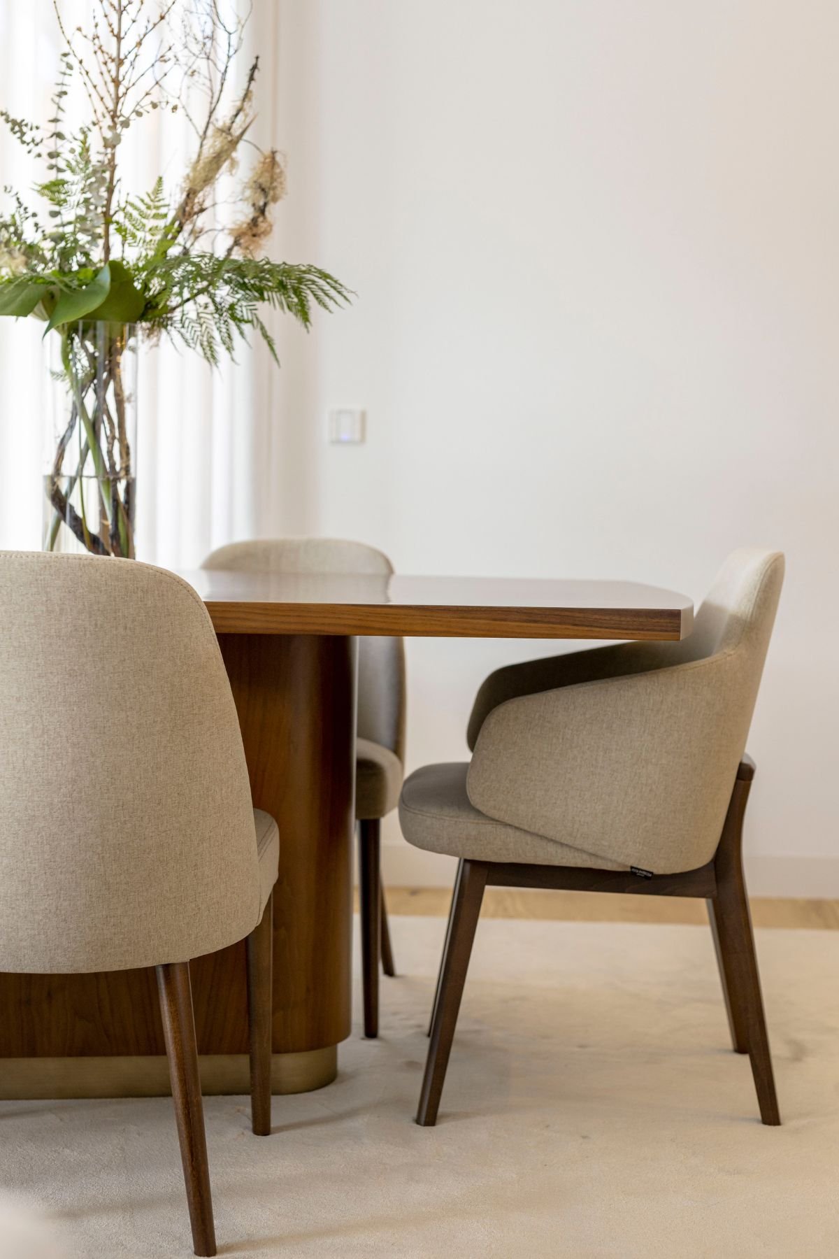 Pormenor do design nórdico das cadeiras com estrutura em nogueira e estofo creme, em harmonia com a mesa e arranjo floral.