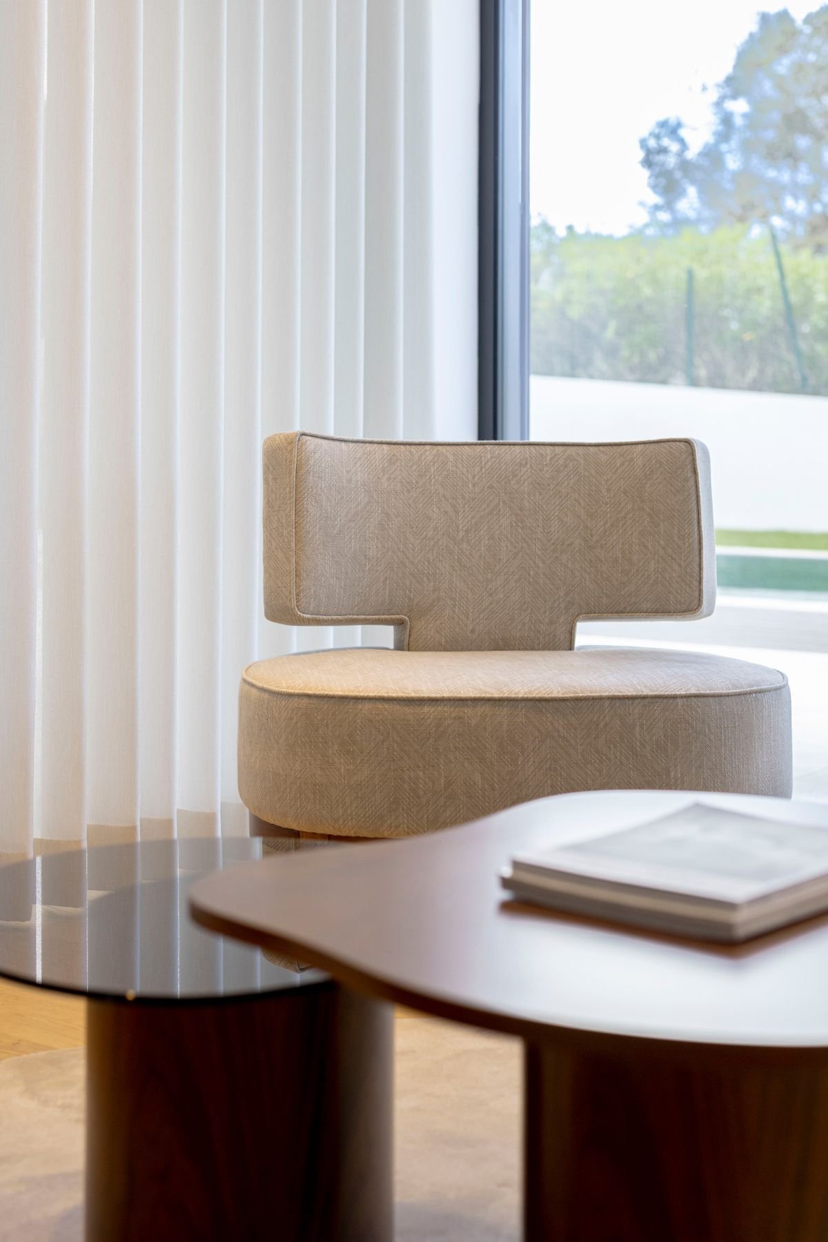 Pormenor do cadeirão de design moderno e tom neutro, evidenciando o seu encosto ergonómico em conjunto com a mesa de apoio.
