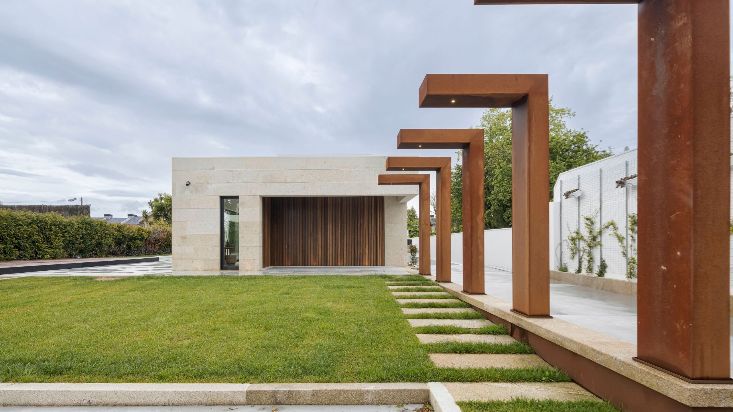 Exterior de casa moderna com pórticos em aço corten e jardim relvado, evidenciando a arquitetura contemporânea e exclusiva típica de casas de luxo.